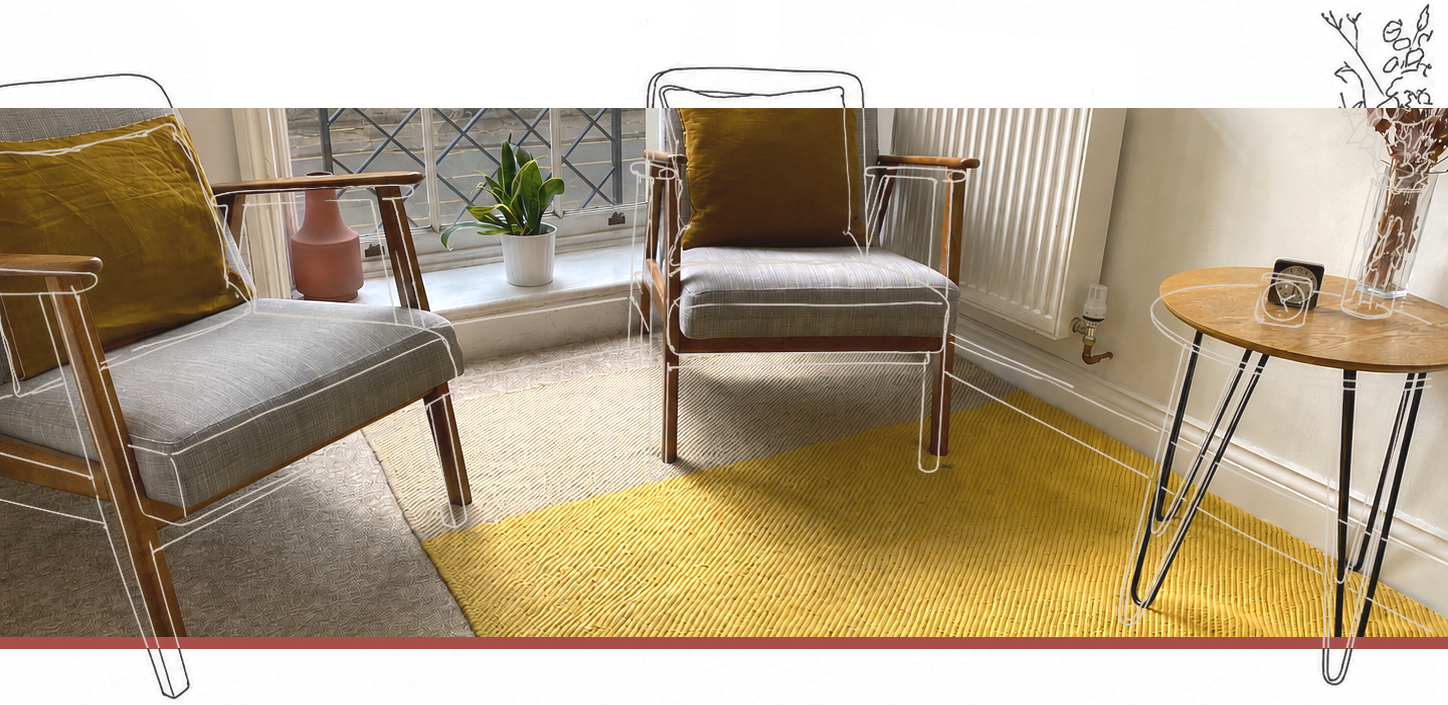 A comfortable looking therapy room containing two empty chairs and a table. On the table are some flowers and a small clock, and the room is brightly lit by the large, Georgian window.