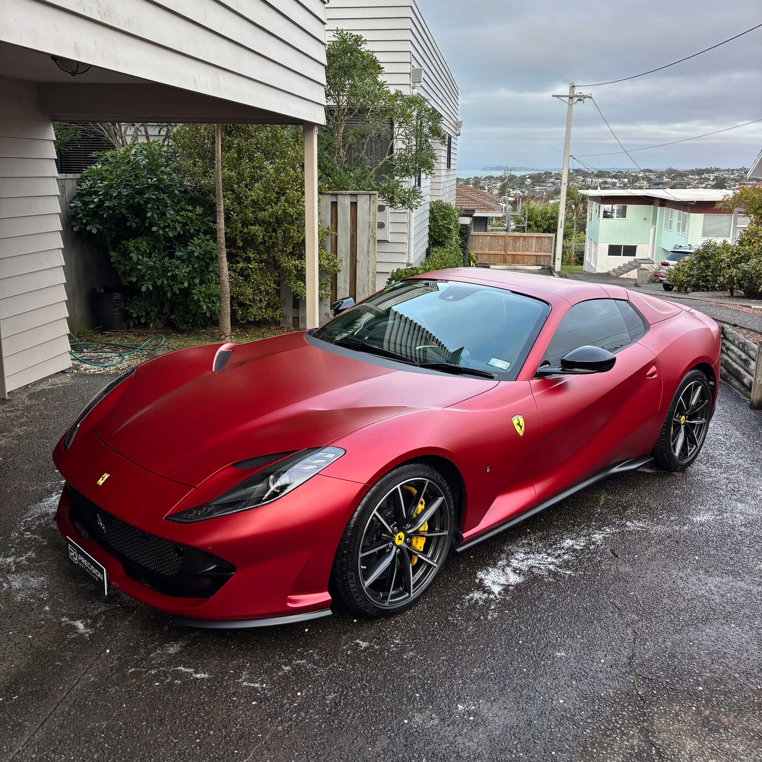Red Ferrari sports car parked in a driveway with houses and a view of the city in the background.