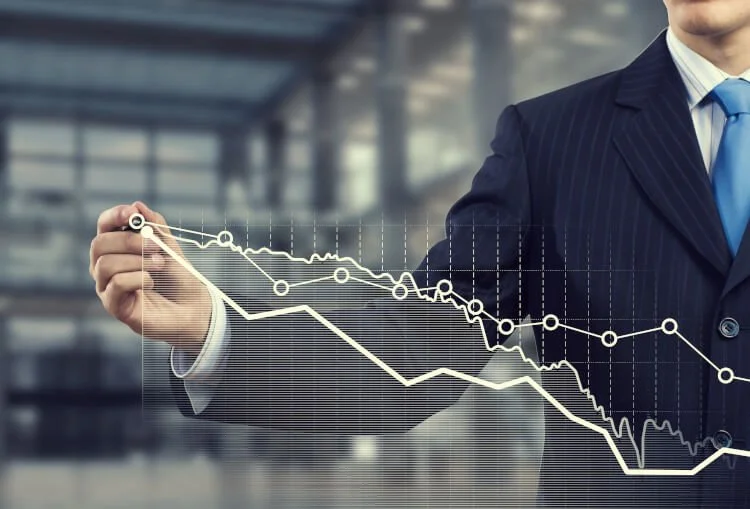 A businessman in a suit drawing declining stock or financial graphs on a transparent screen.