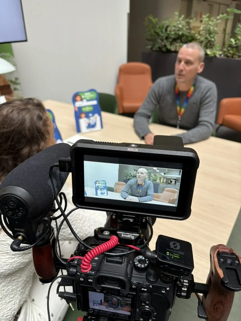 een interviewsetting met een man die tegenover een meisje zit, terwijl een videocamera opnames maakt