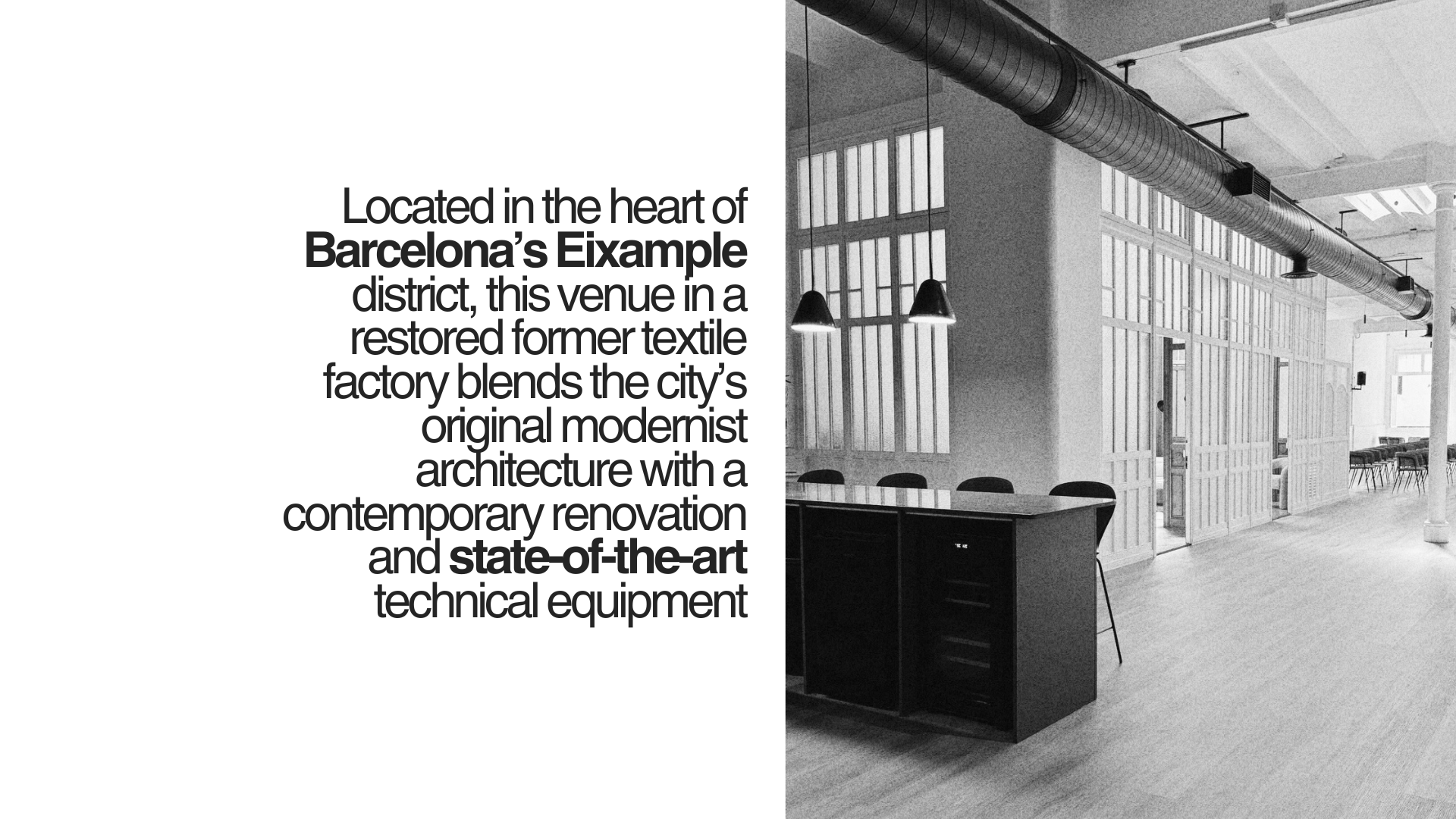 Black and white photo of a modern interior space with industrial design, featuring large windows, hanging lights, exposed ductwork, and a seating area with chairs in the background.