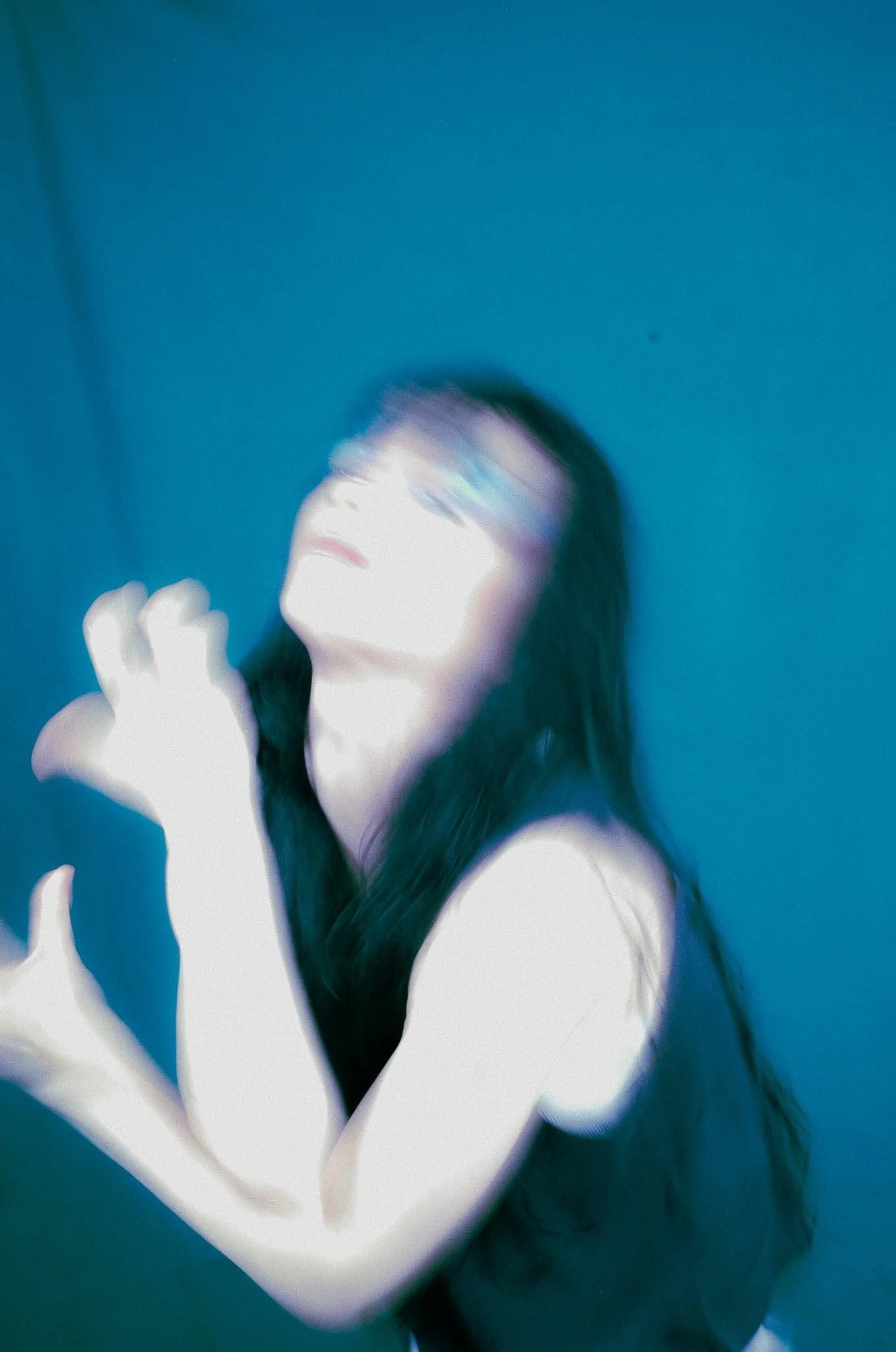 Abstract photo of a person with long dark hair, holding their hand up with fingers close together, against a blue background with motion blur and distortions.