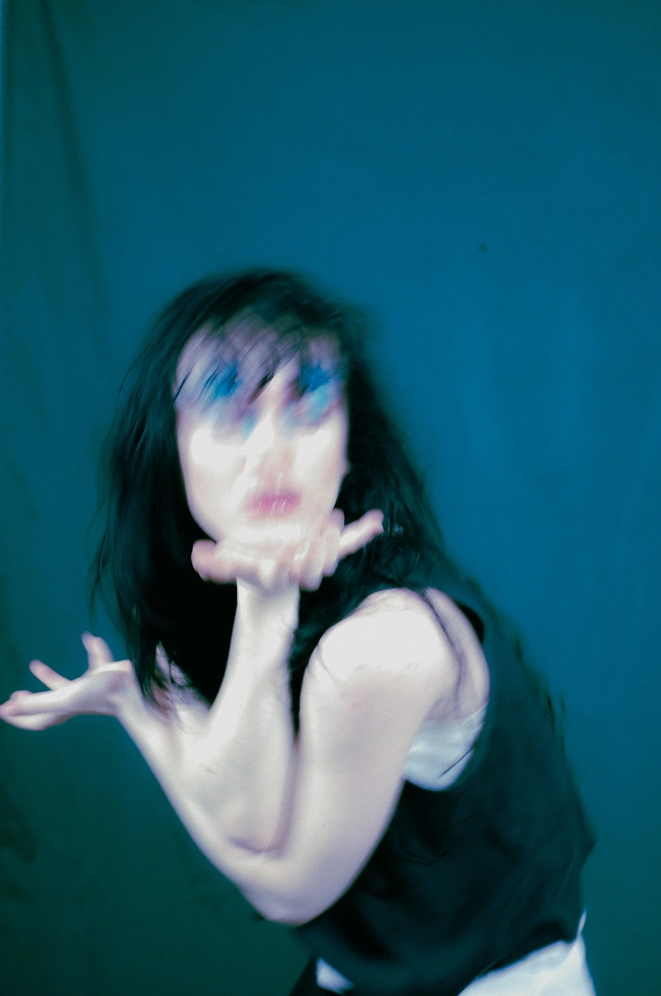 A woman with black hair and glasses is in motion, striking a dance pose against a dark background.