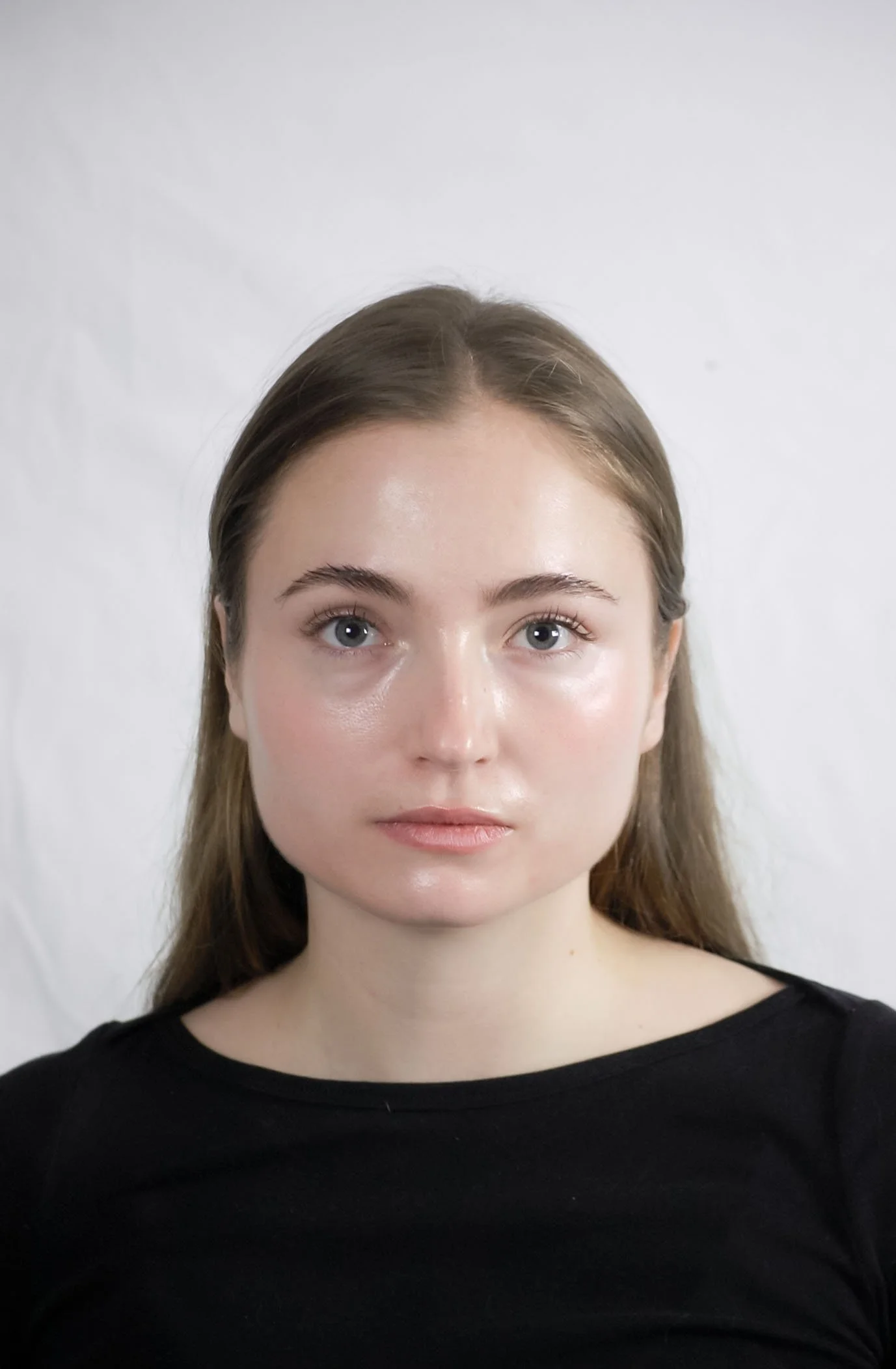 A young woman with long brown hair and blue eyes wearing a black shirt against a plain white background.