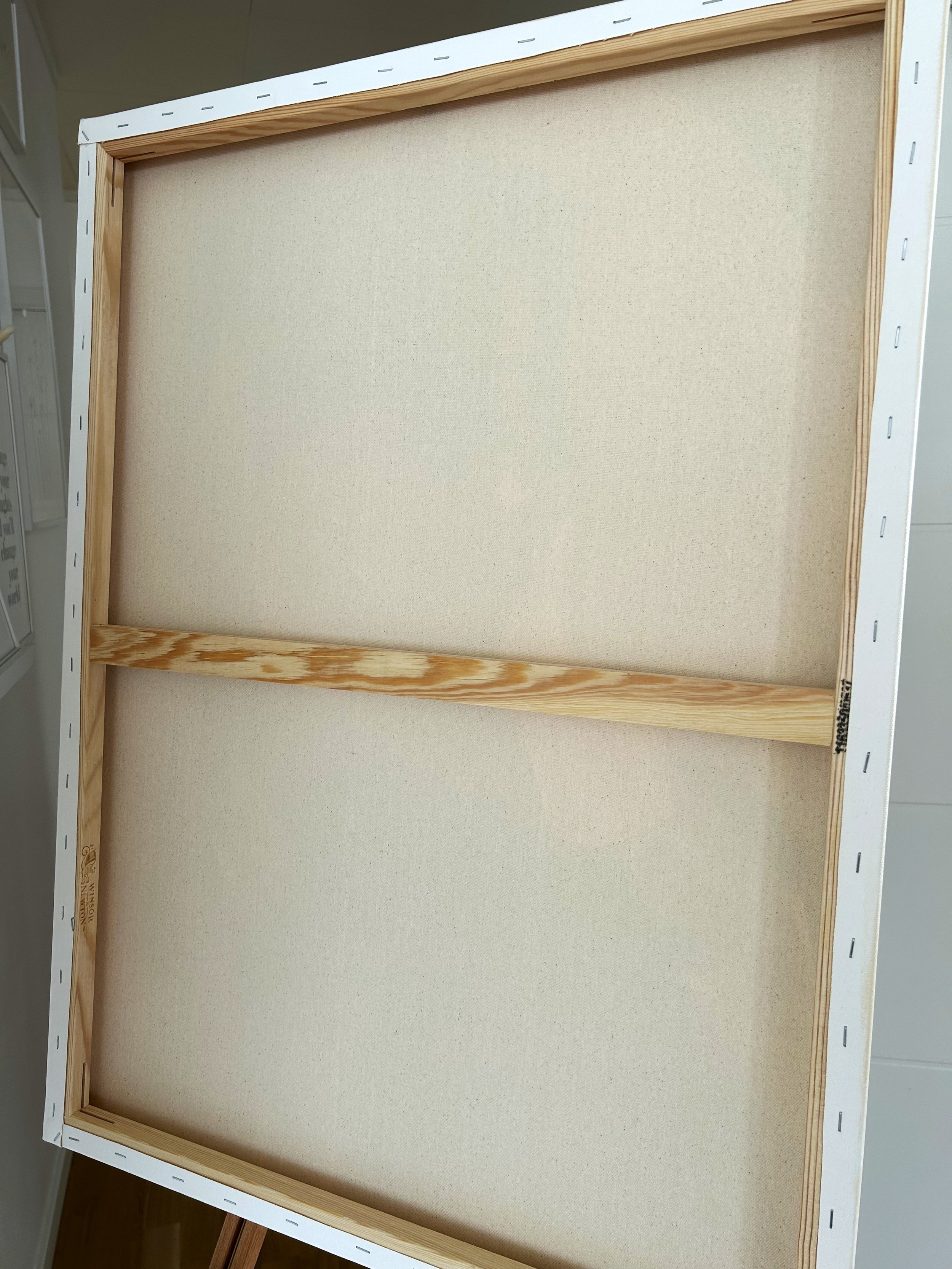 Back view of a stretched cotton canvas showing the wooden stretcher frame, central support bar and staples around the edges.