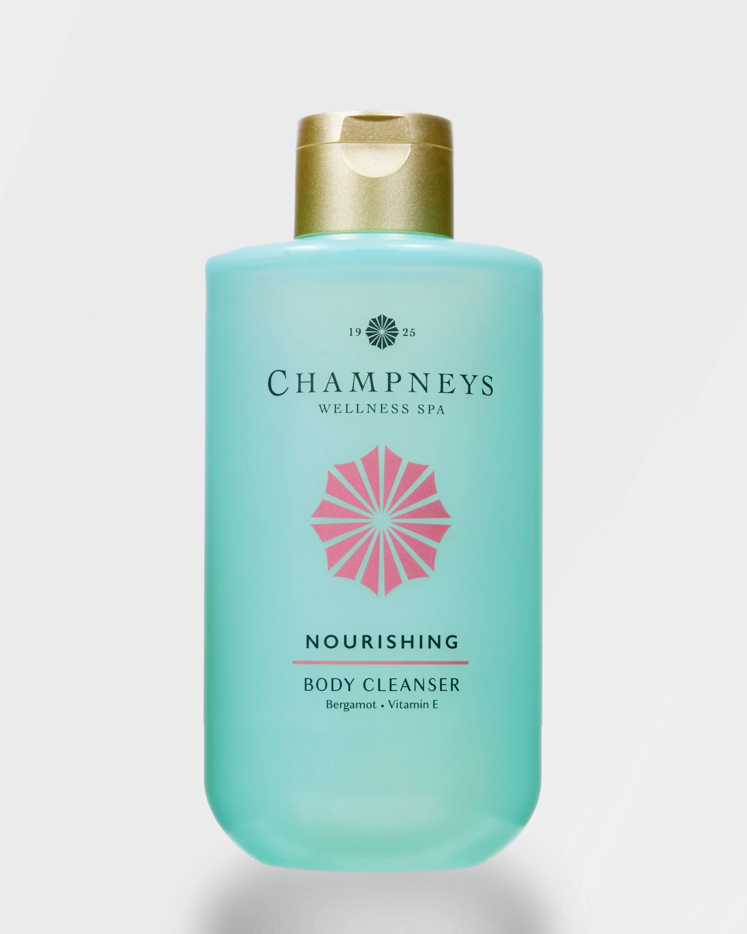 Light blue bottle of Champneys Wellness Spa Nourishing Body Cleanser with gold cap, label features a pink geometric flower, bergamot, and vitamin E.