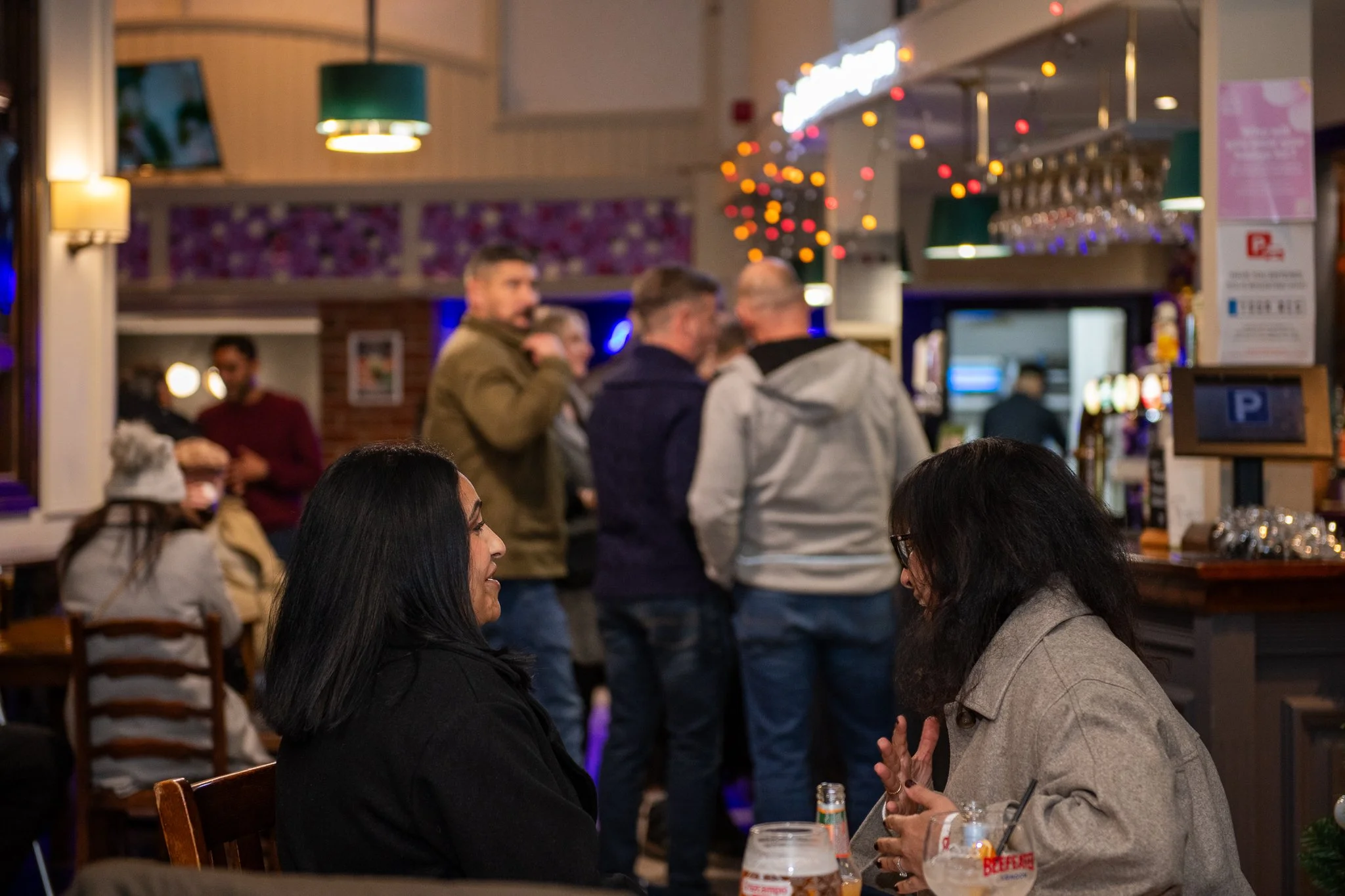 People socializing in a lively bar or restaurant with festive string lights and colorful decor.