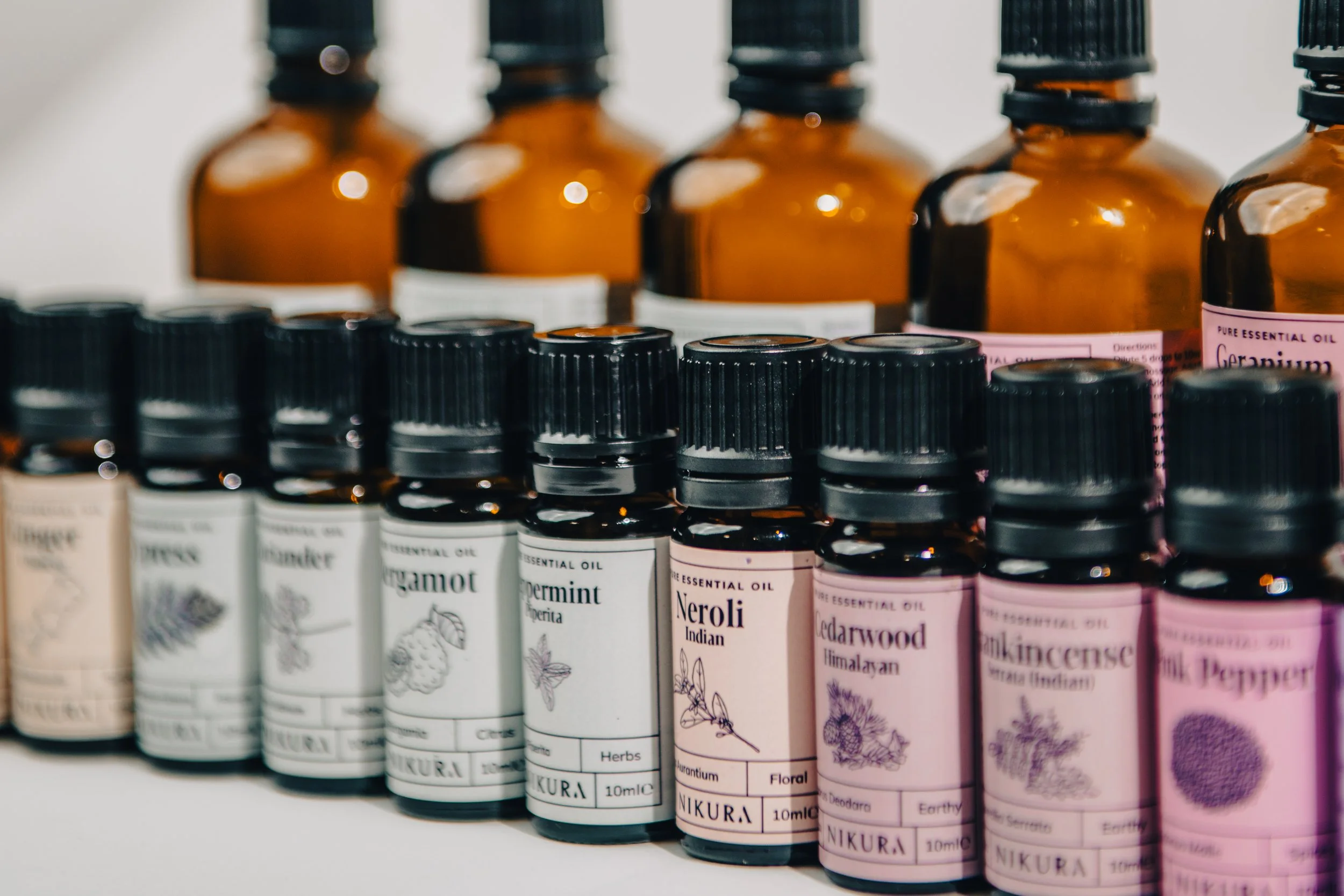 Several small bottles of essential oils with black caps and pastel pink labels aligned on a shelf.