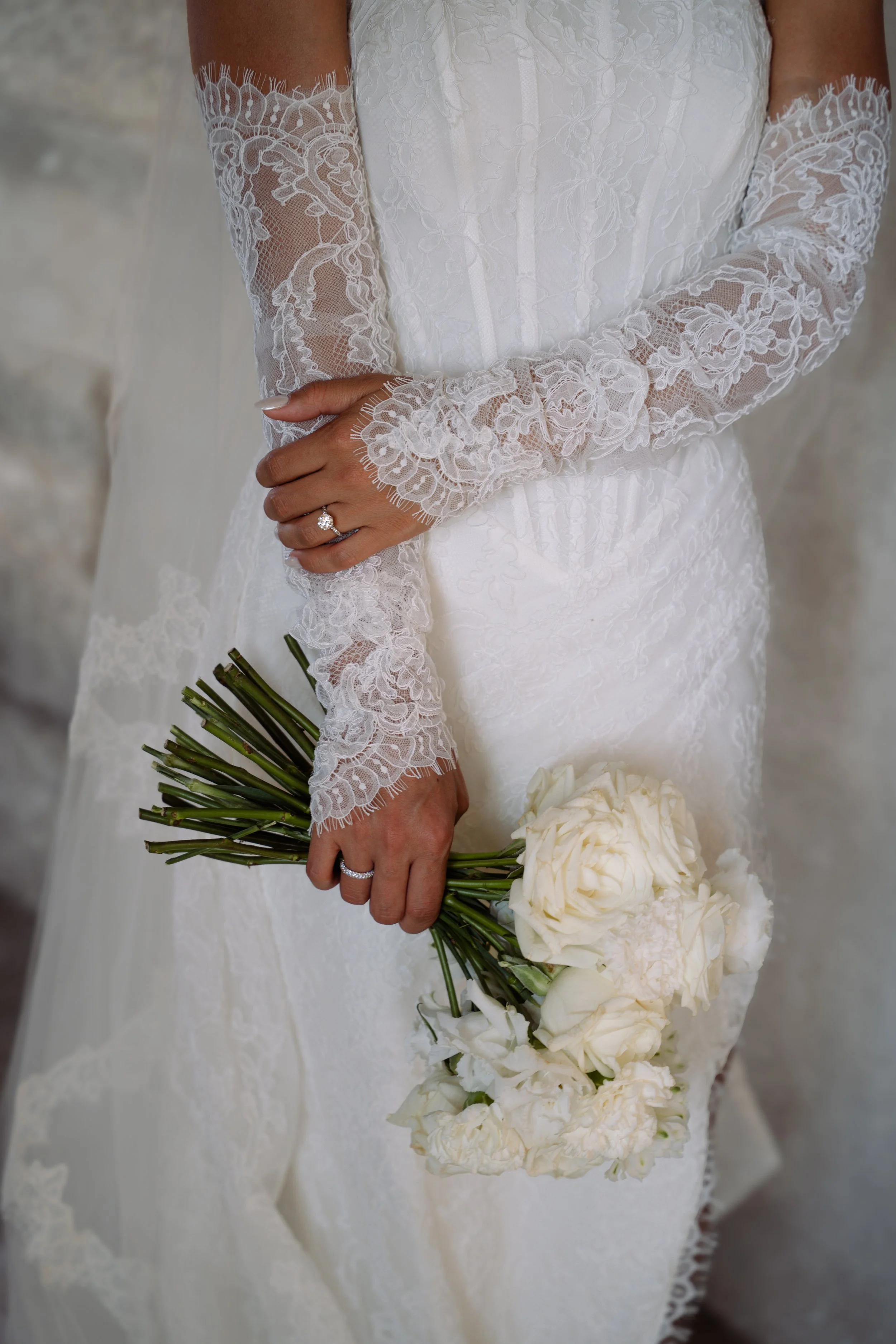 Close-up of a bride in a white lace wedding dress holding a bouquet of white flowers.