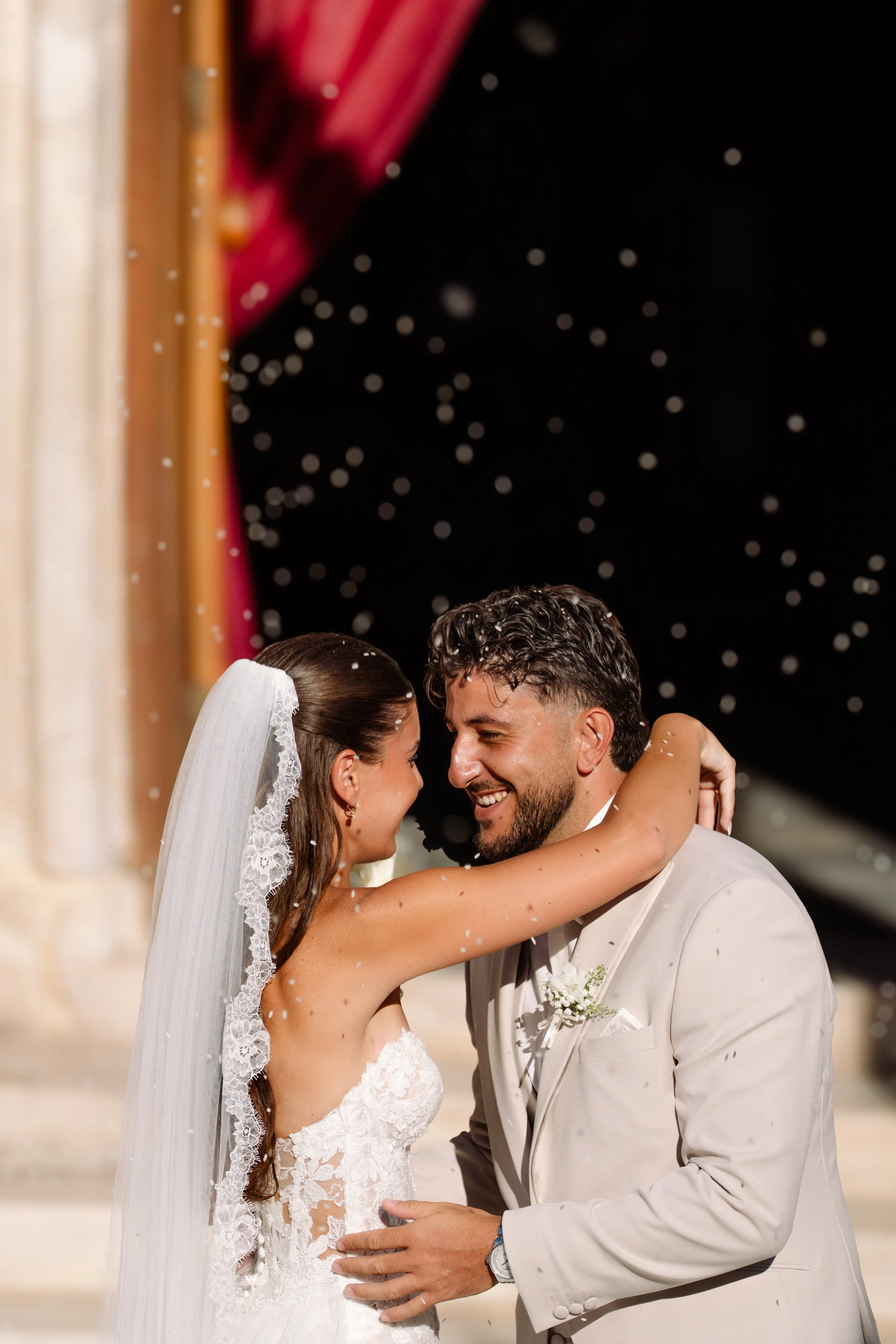 A bride and groom lovingly embrace and smile at each other during their wedding celebration, surrounded by falling confetti.