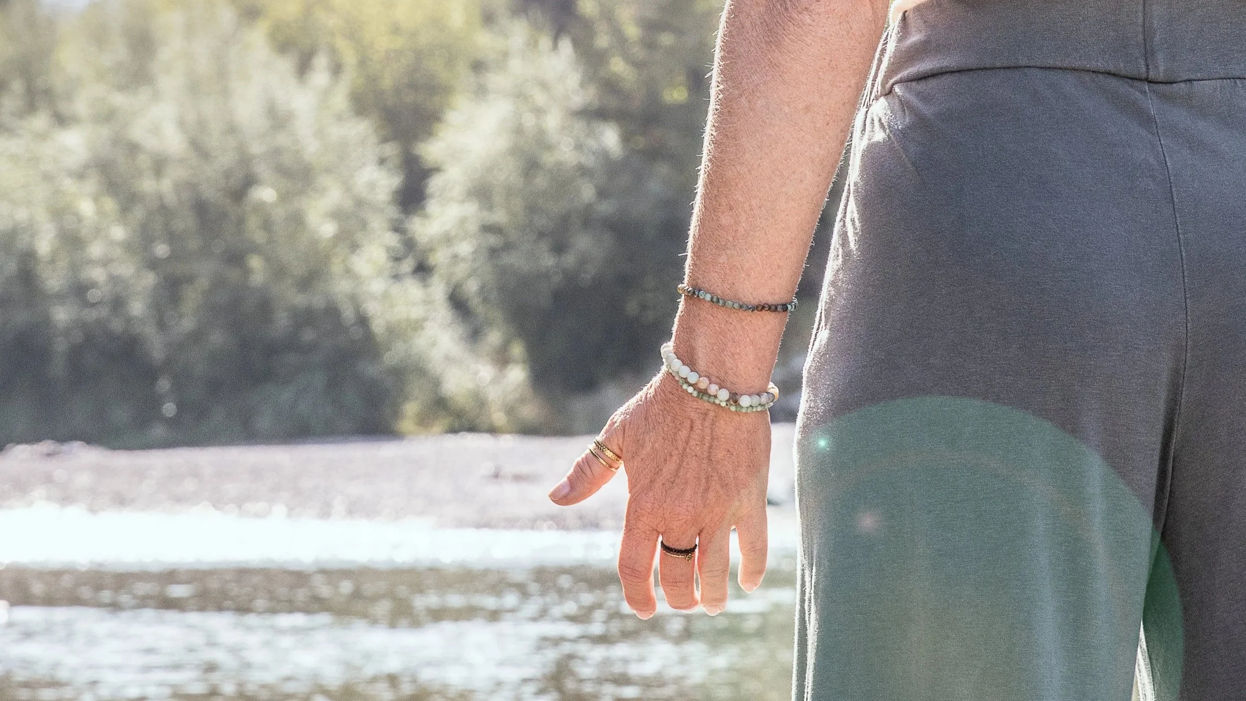 Nahaufnahme der Hand einer Person, die dicke Armbänder trägt, bei Sonnenlicht vor natürlicher Hintergrund.