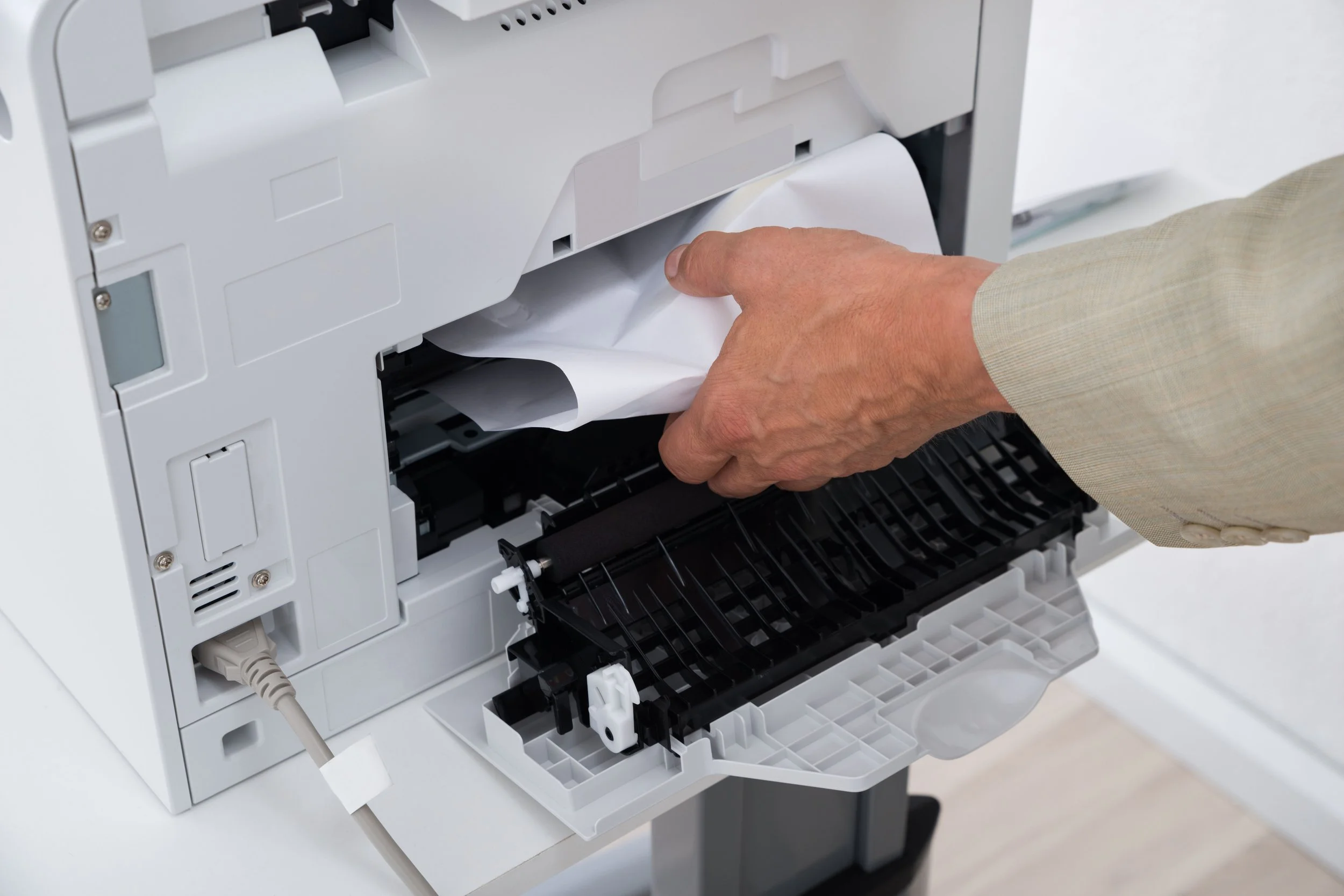 A person wearing a beige suit is pulling out paper from a white multifunction printer or copier machine.