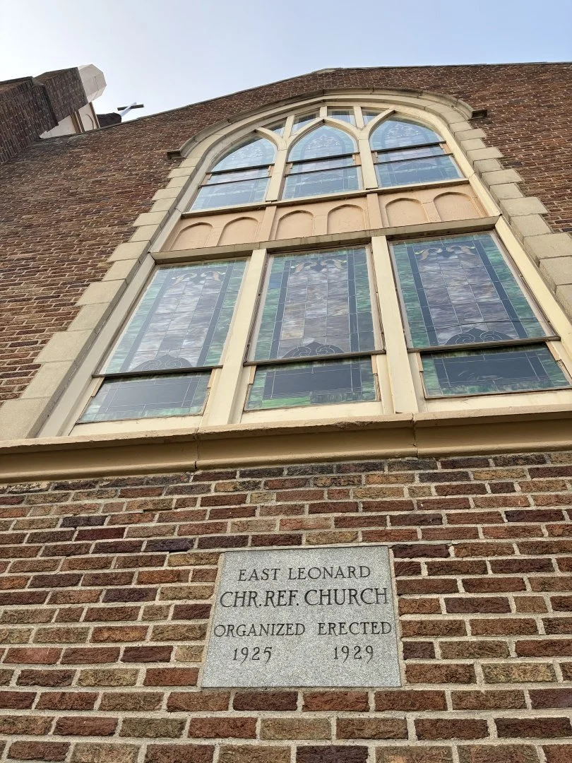 A large stained glass window on the brick exterior of the East Leonard Church, organized and erected between 1925 and 1929.