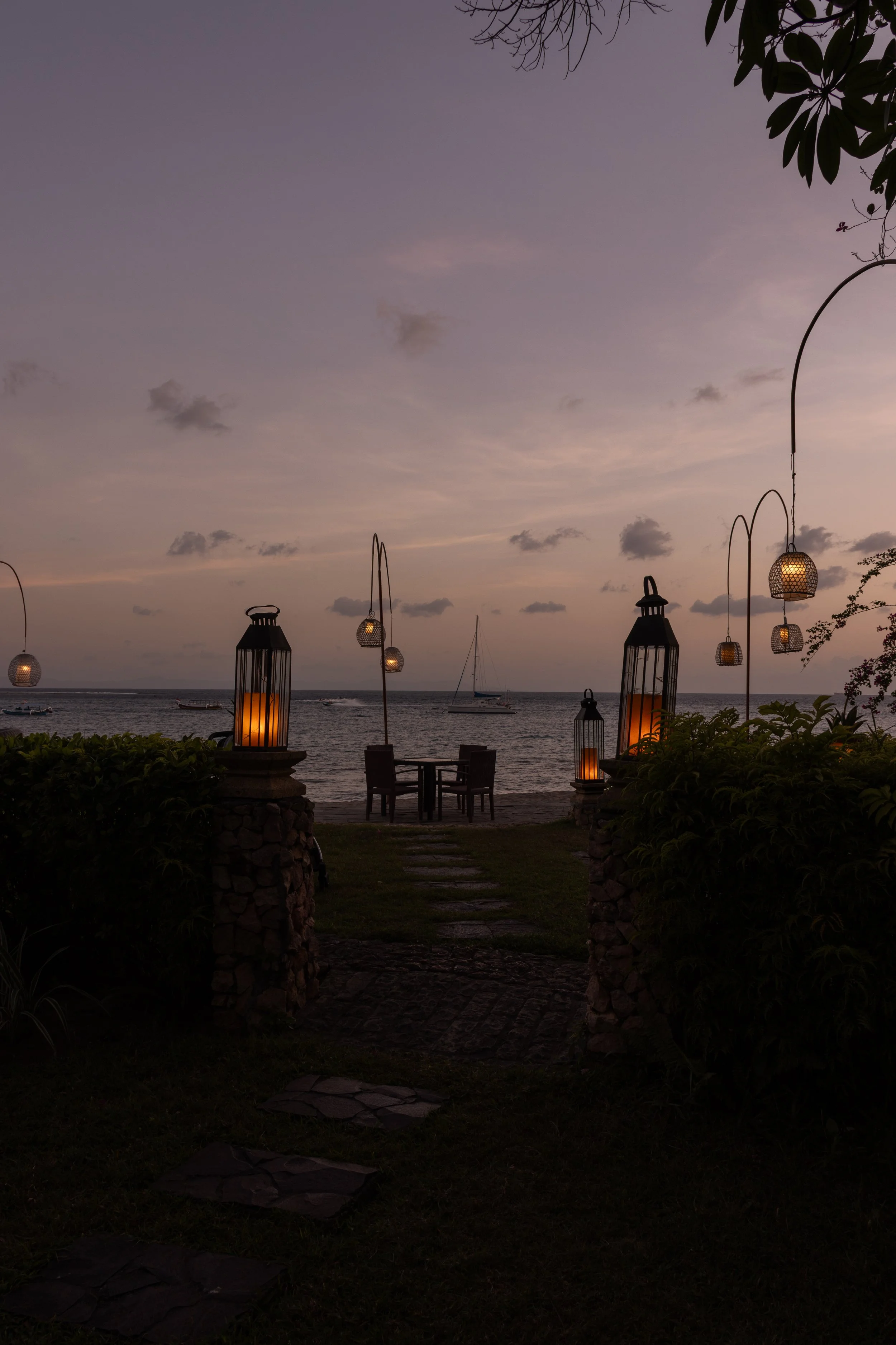 A lantern-lit beach pathway at sunset with boats in the distance, representing the welcoming start of Hayah Reserve's connection process.