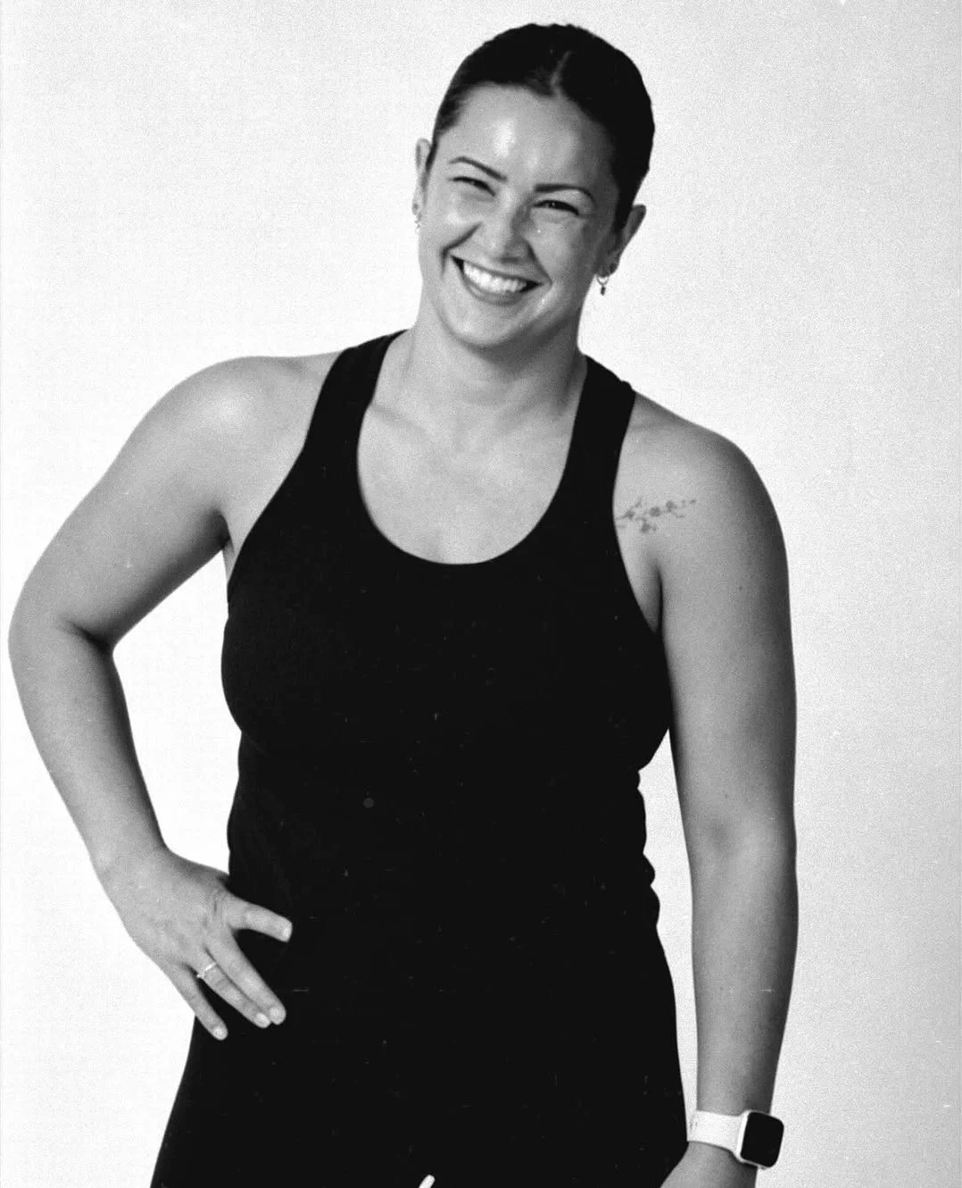Black and white photo of a smiling woman in a sleeveless top, with her hand on her hip, against a plain background.