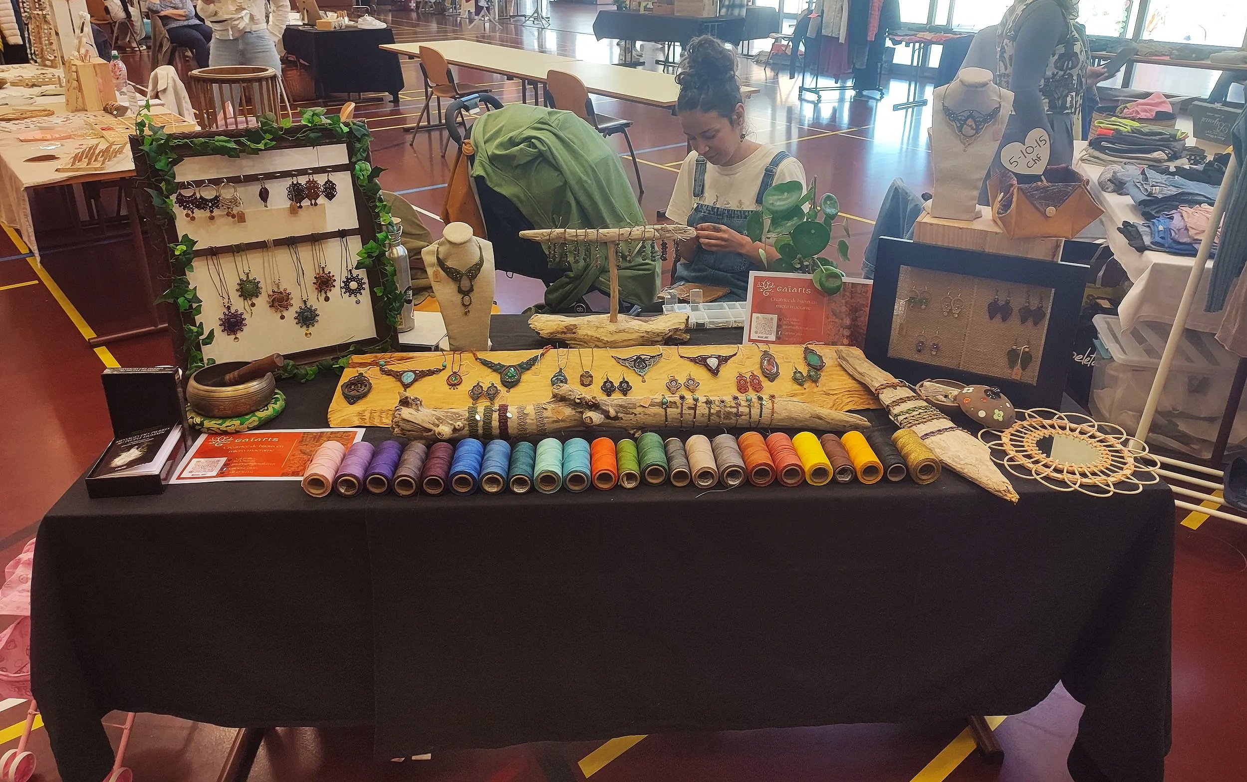 Vente d'artisanat avec bijoux, fil de couture coloré et accessoires de bijoux sur un marché intérieur.