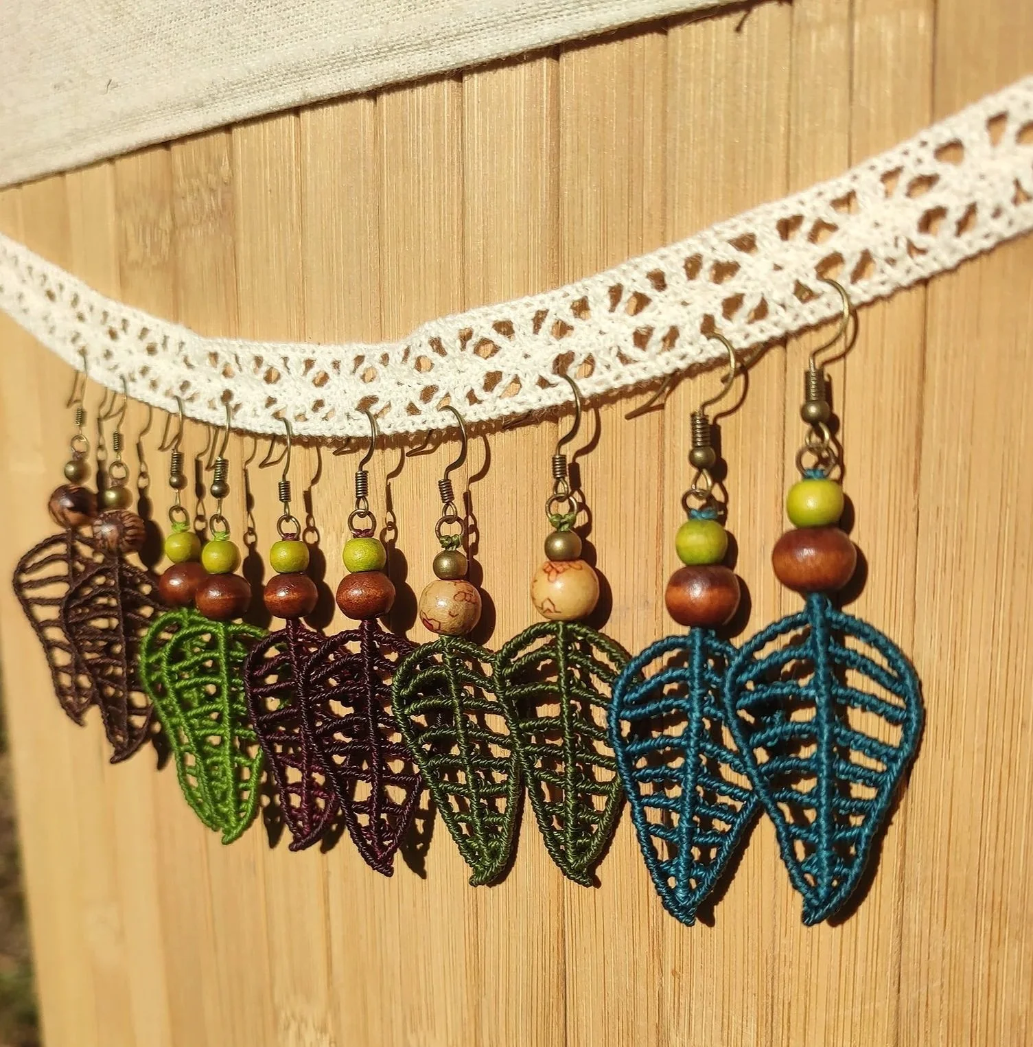Une décoration faite de crochet, avec des feuilles en perles colorées et des pendants en forme de feuilles en fil crocheté multicolore, suspendus à un ruban de crochet blanc fixé au mur.