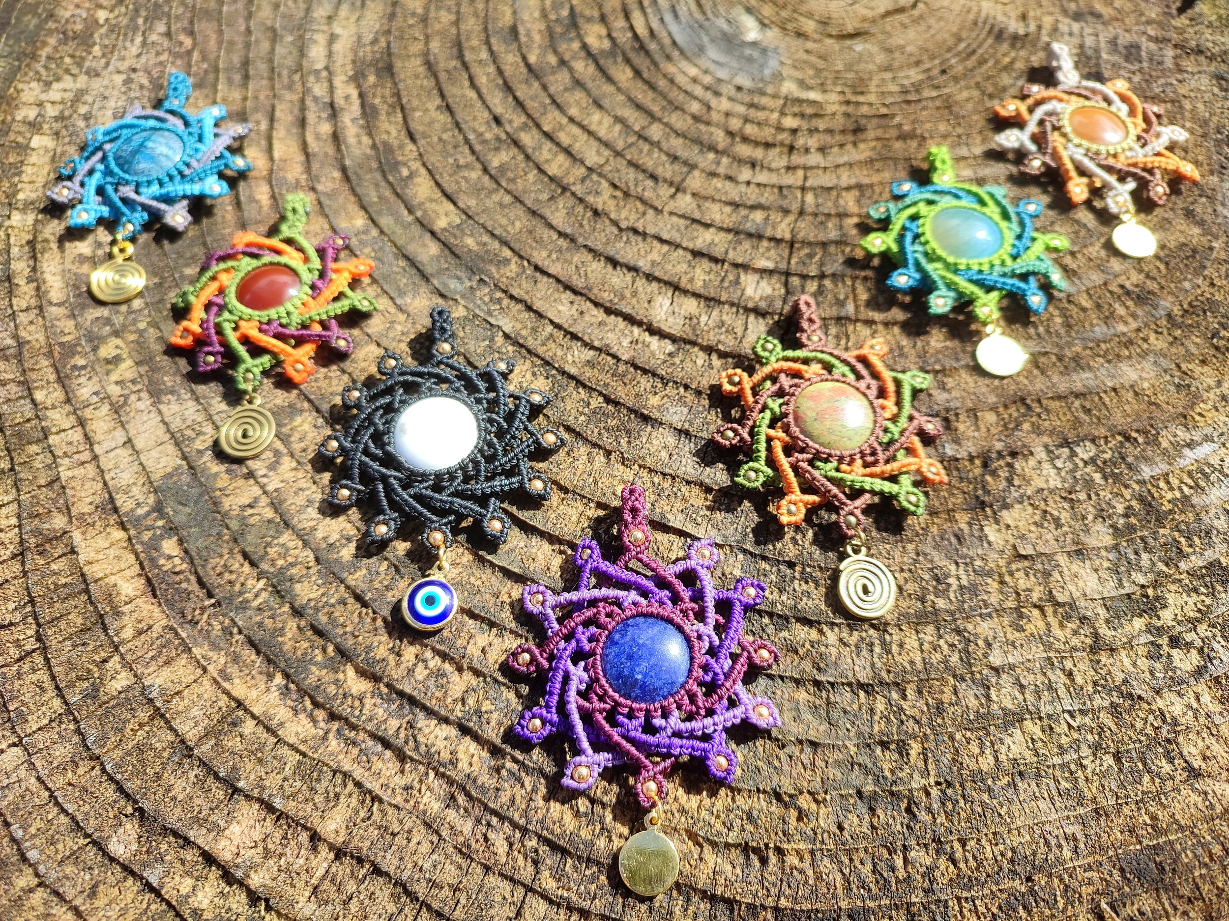 Des pendentifs colorés en macramé, ornés de pierres et de pièces métalliques, posés sur une surface en bois.