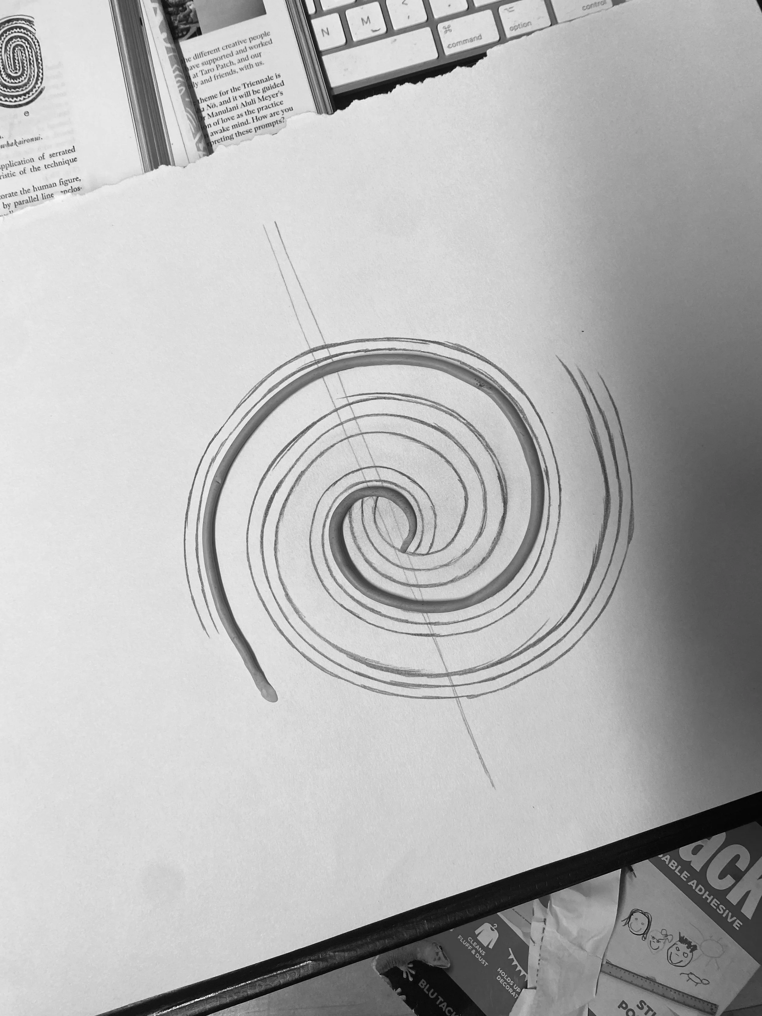 A torn piece of paper with a spiral design drawn on it, placed on an office desk near a keyboard and scattered papers.