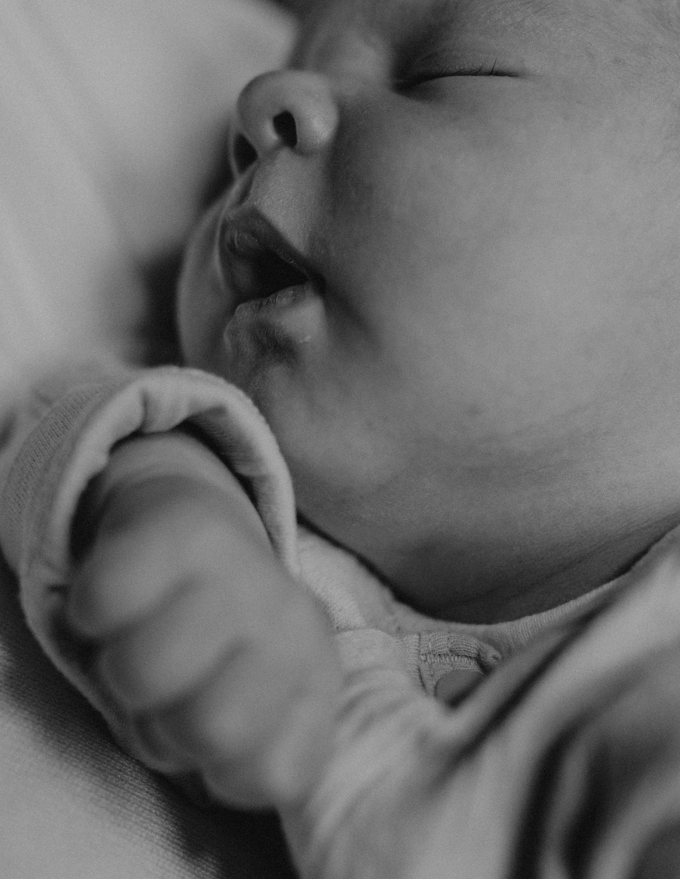 Close-up black and white photo of a sleeping baby's face, focusing on the nose and closed eye, with soft lighting and gentle shadows.