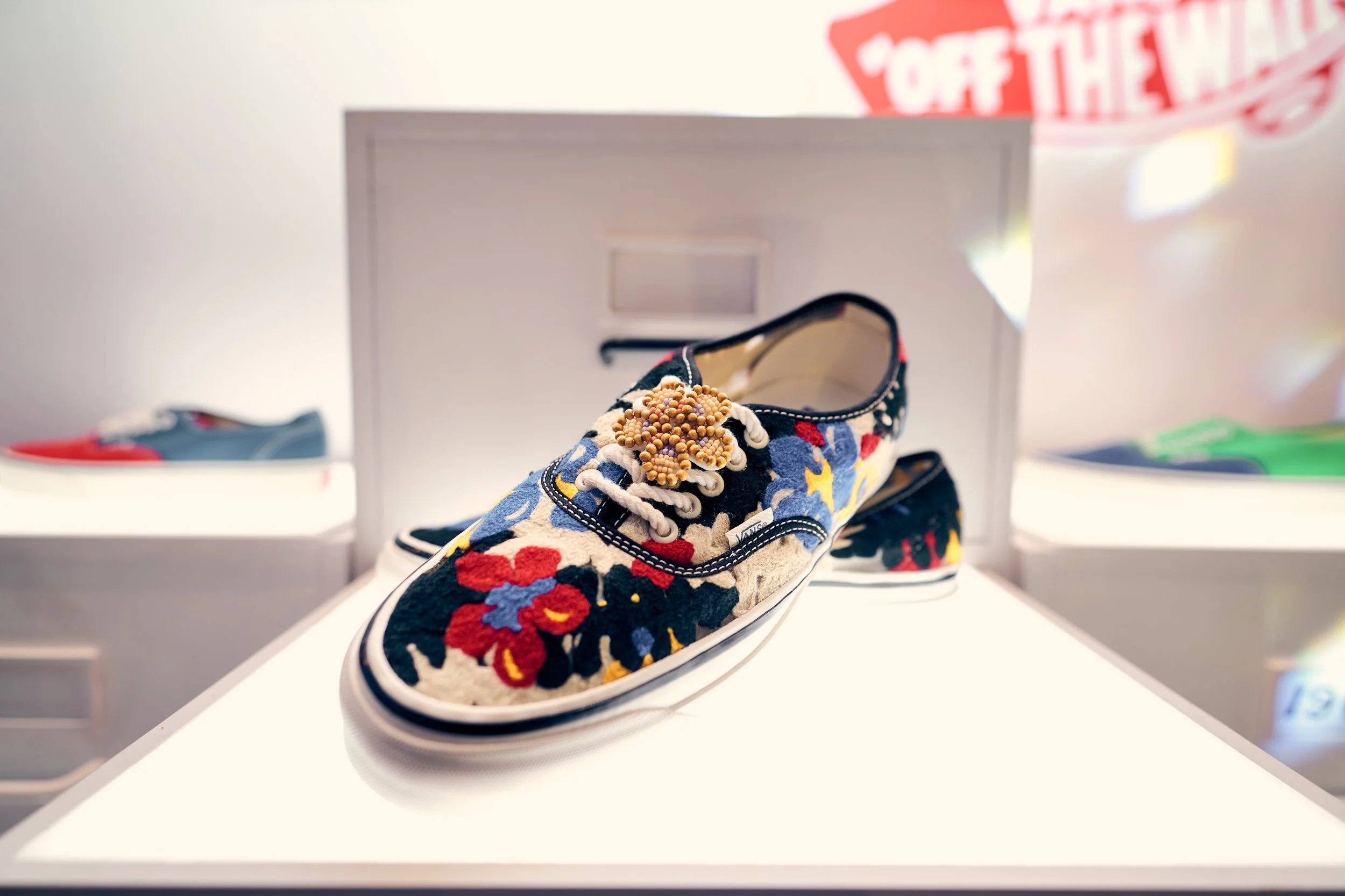 A colorful sneaker with floral embroidery and bead embellishments on display in a store.