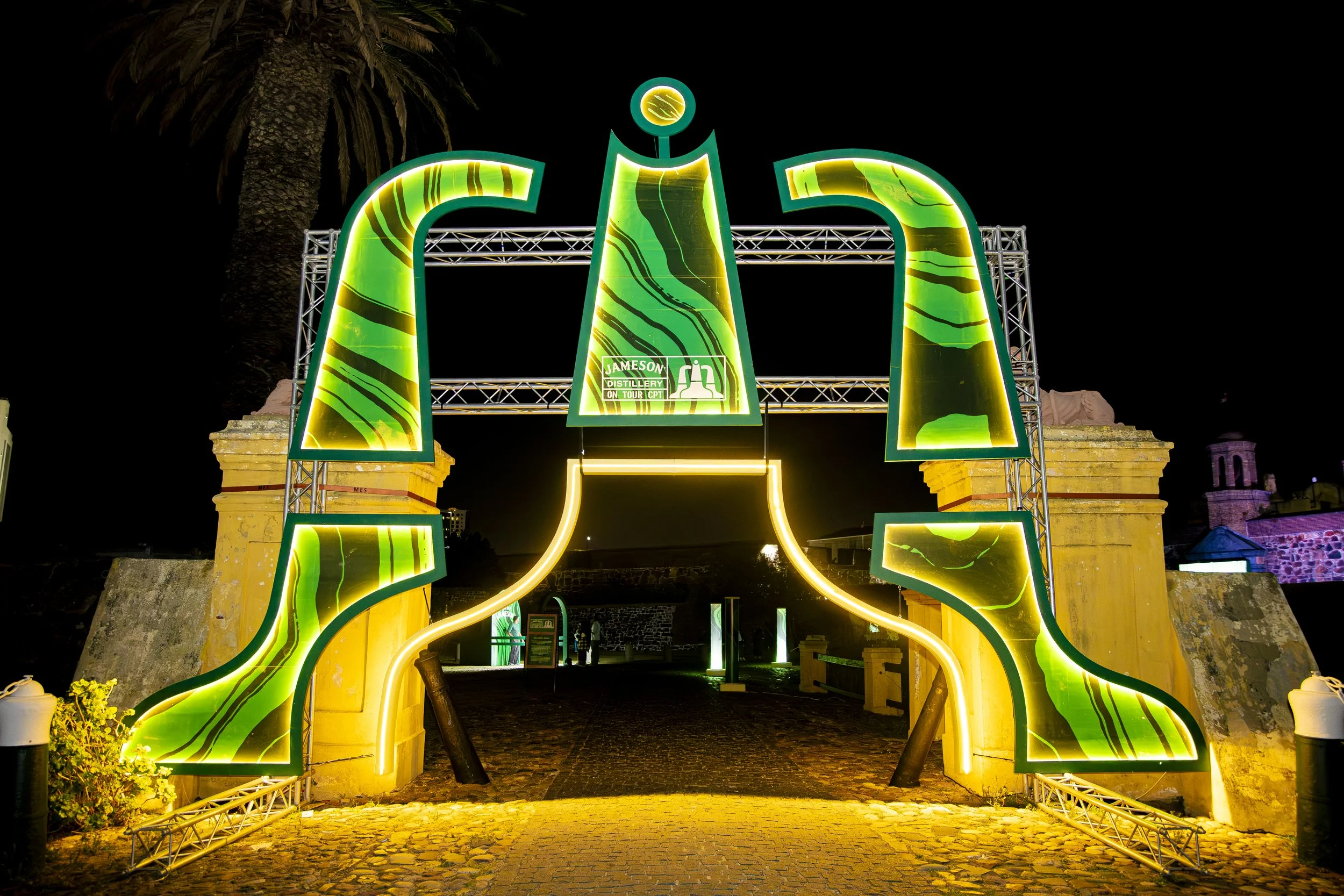Colorful illuminated archway at night with a sign for Jameson distillery on tour, set against a dark sky and historic buildings in the background.