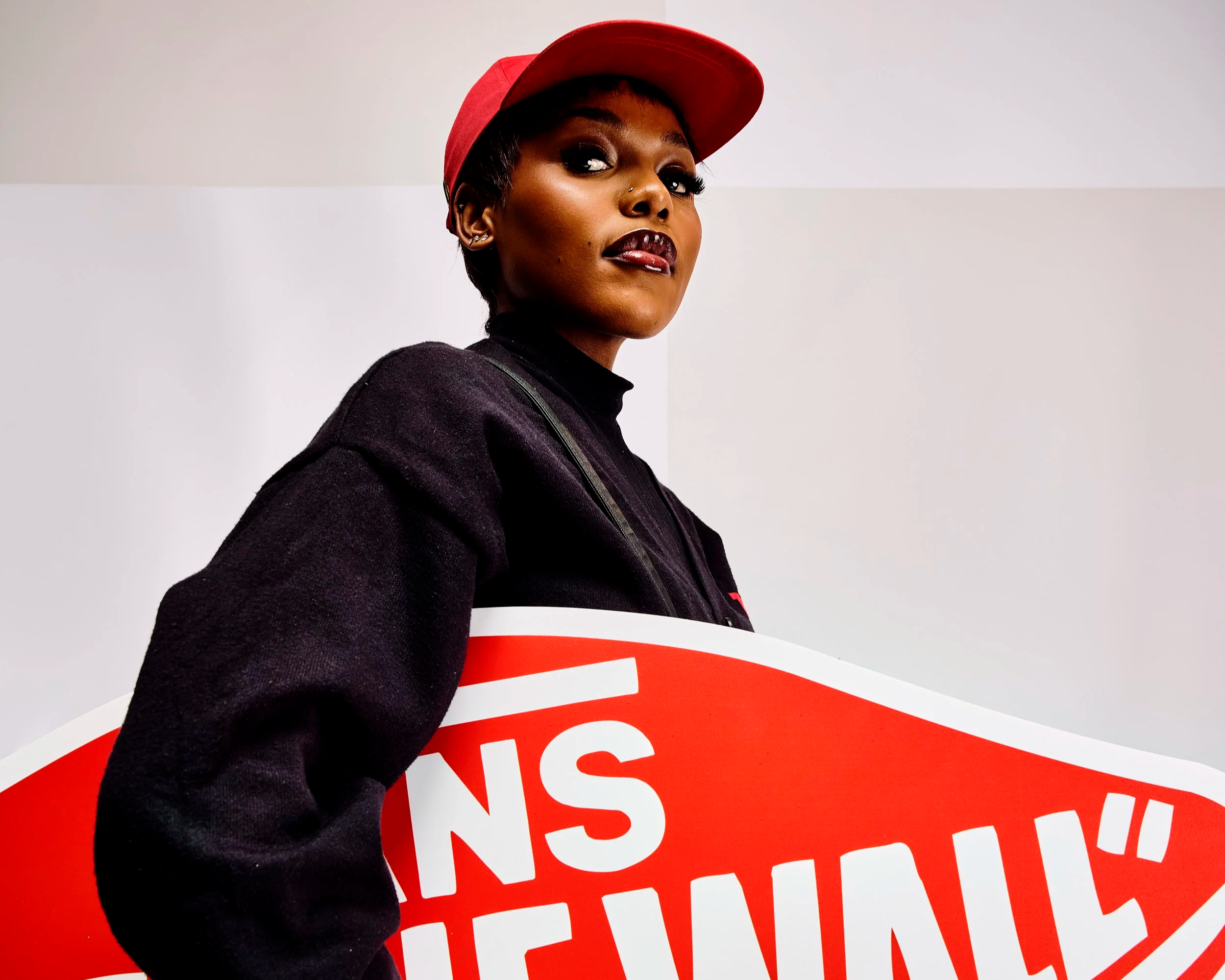 A woman wearing a red cap and dark clothing is holding a large red and white protest sign that says 'STOP THE HATE.'
