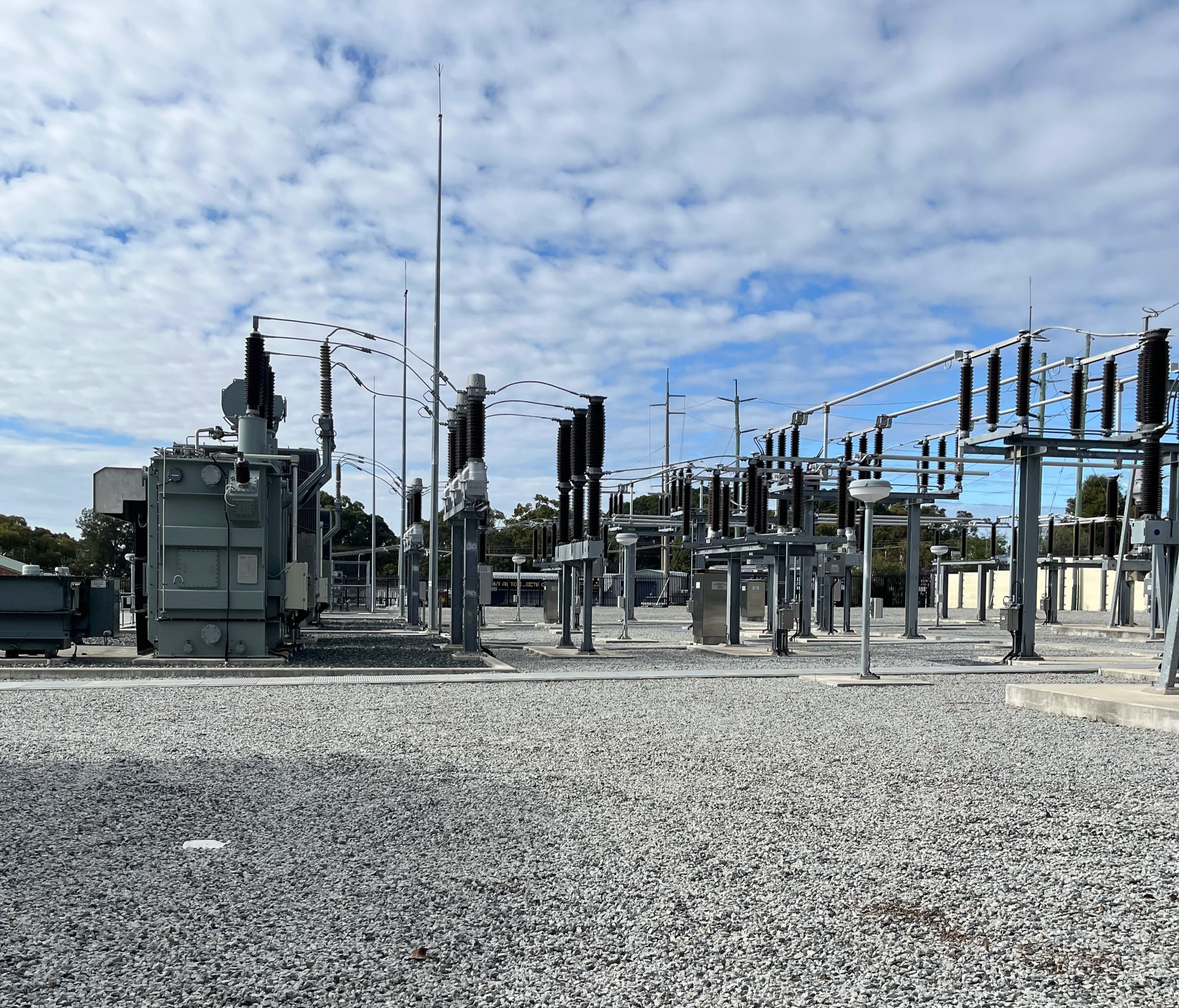 A power substation with electrical equipment and insulators against a partly cloudy sky.