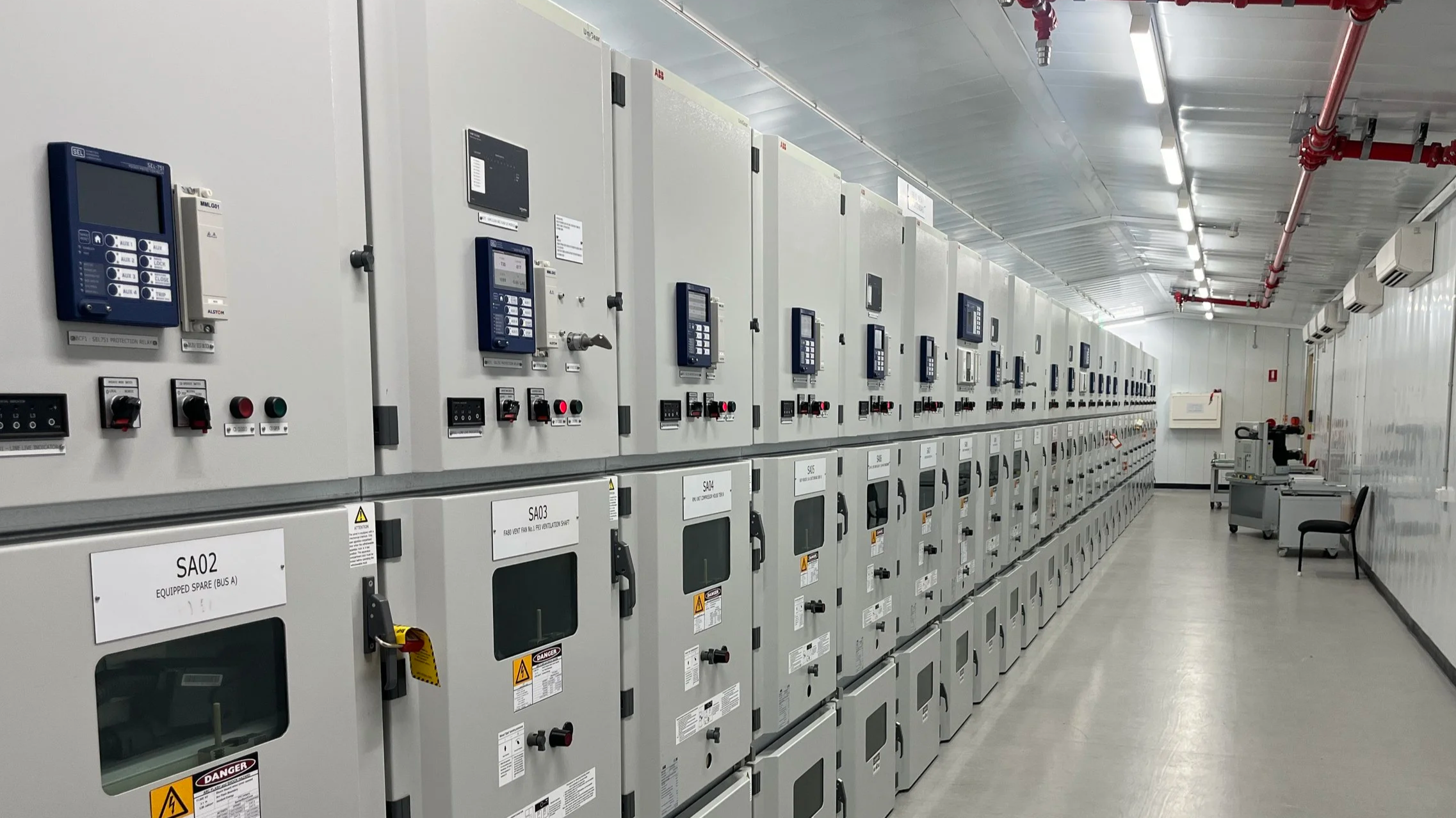 A room filled with rows of electrical control panels or switchgear cabinets with digital displays, switches, and labels.
