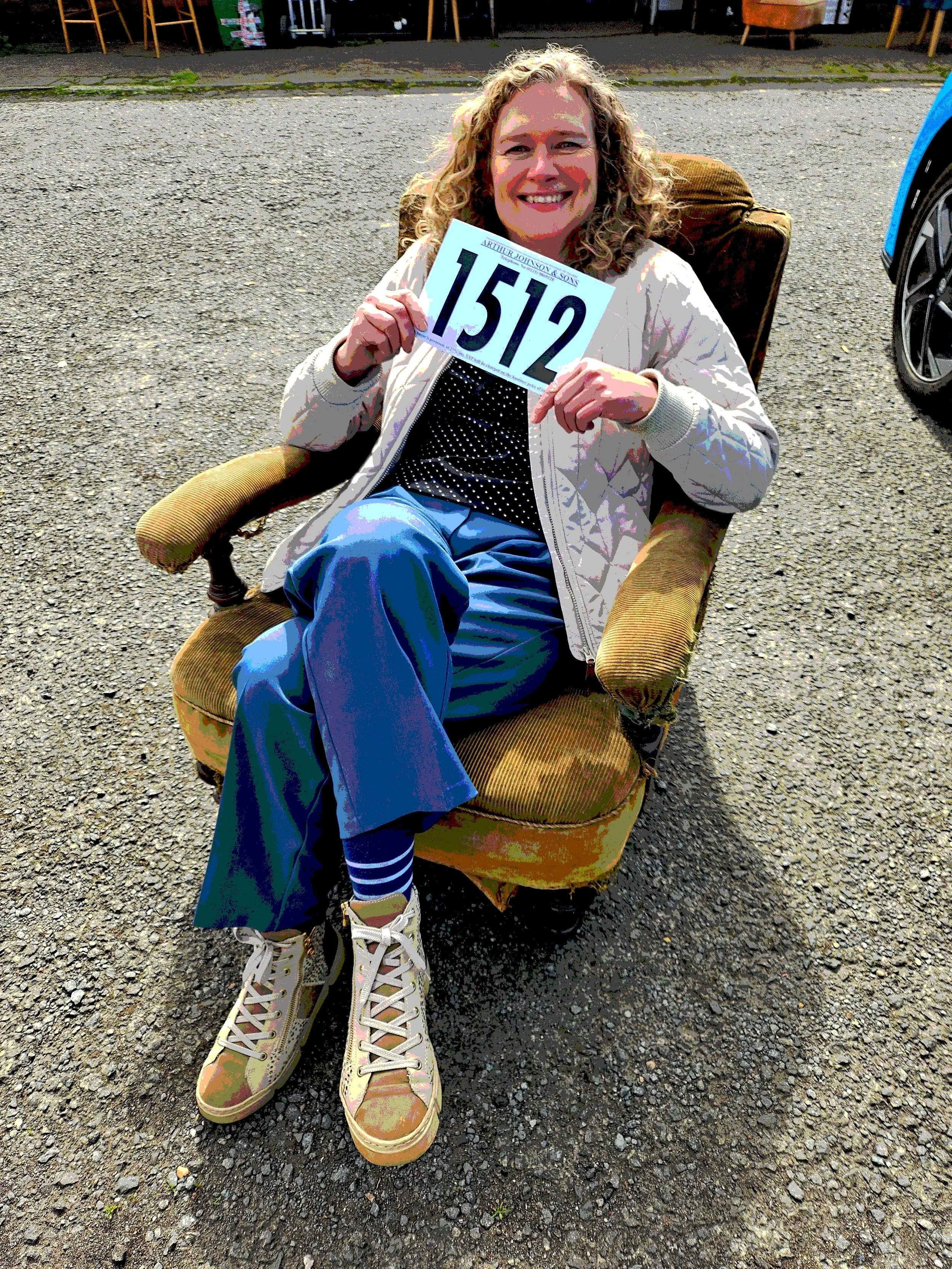 woman smiling holding auction number in antique chair