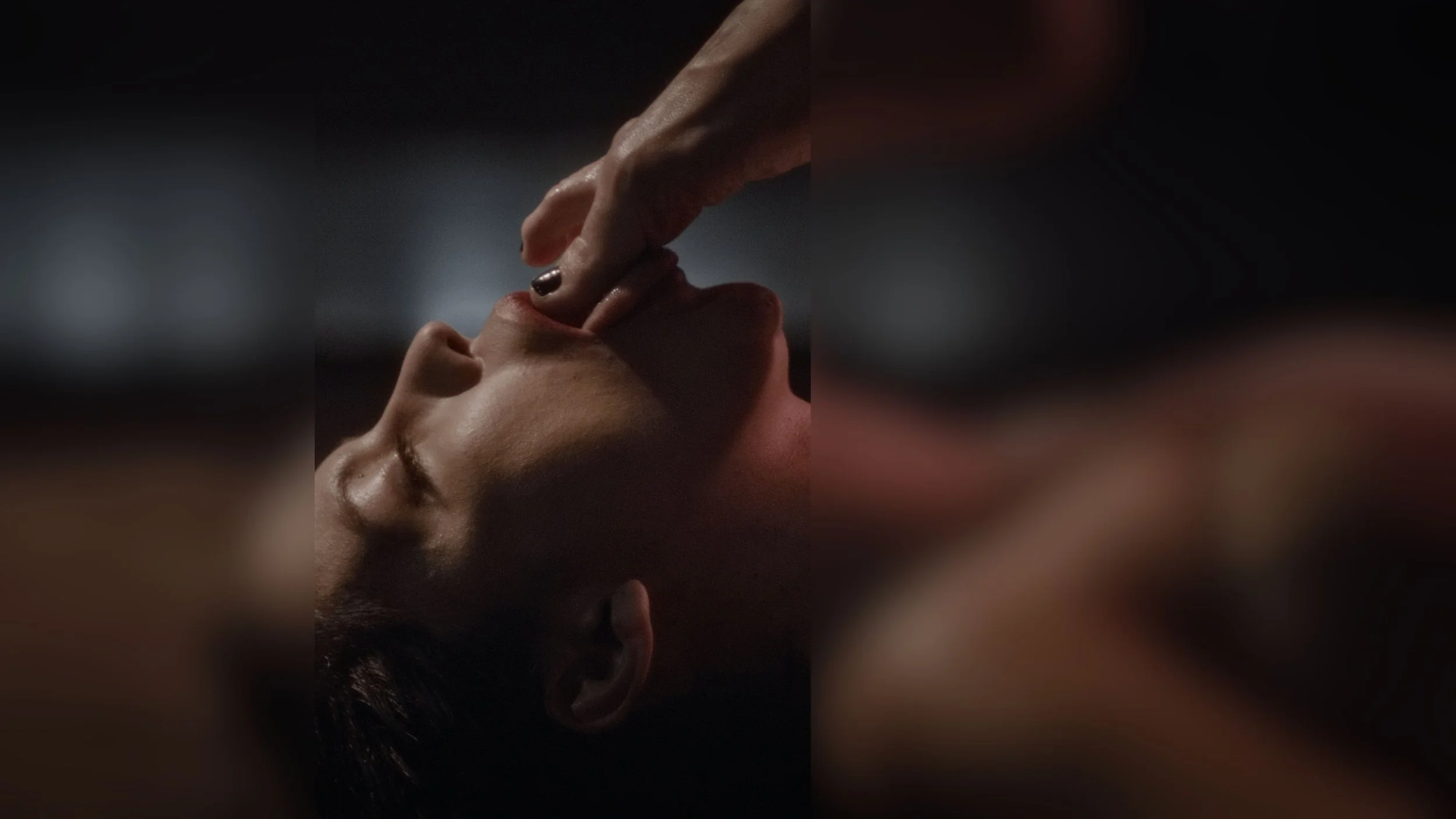 Close-up of a person lying down with their eyes closed, receiving a gentle touch on their chin with their finger.