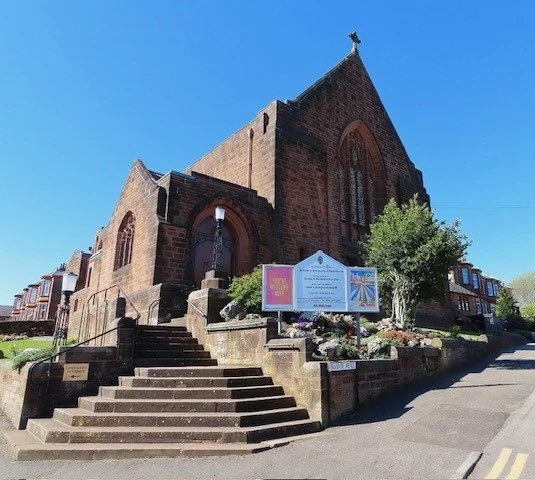 A historic brick church with a steep roof and steps leading up to the entrance, situated on a street with residential buildings.