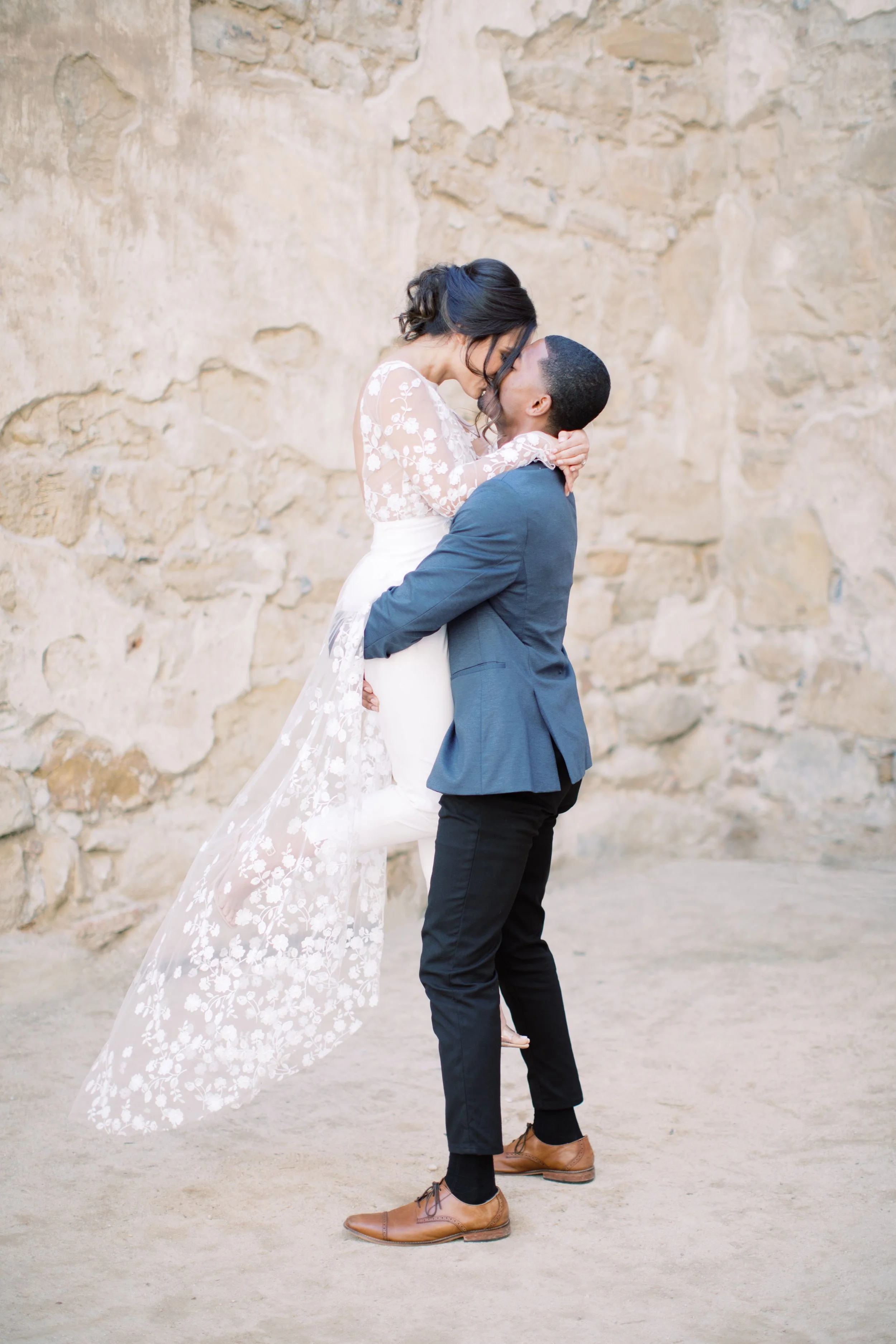 Brautpaar in Hochzeitskleidung bei einem innigen Moment vor einer Natursteinmauer in Portugal