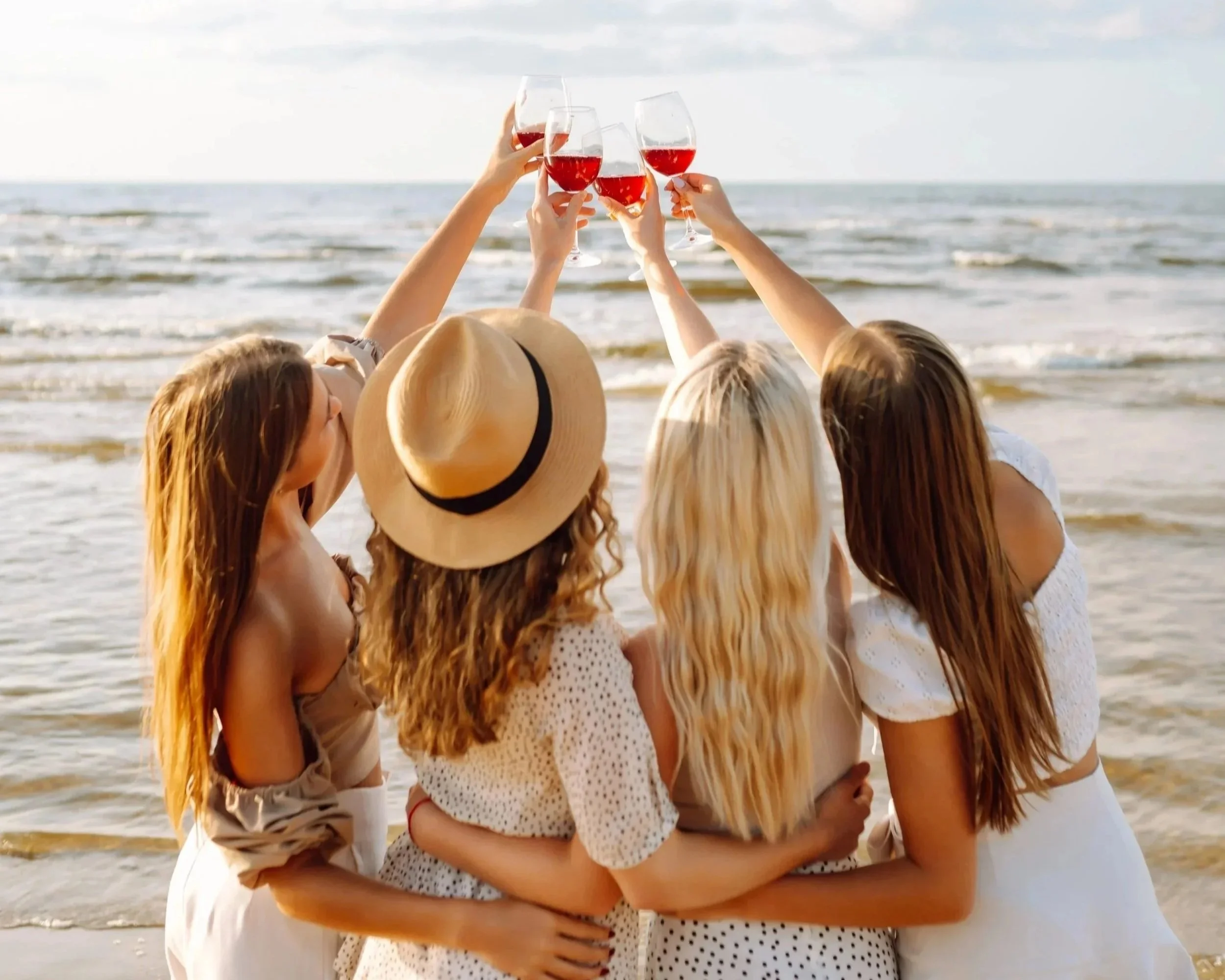 Group of friends at the beach raising glasses of red wine.