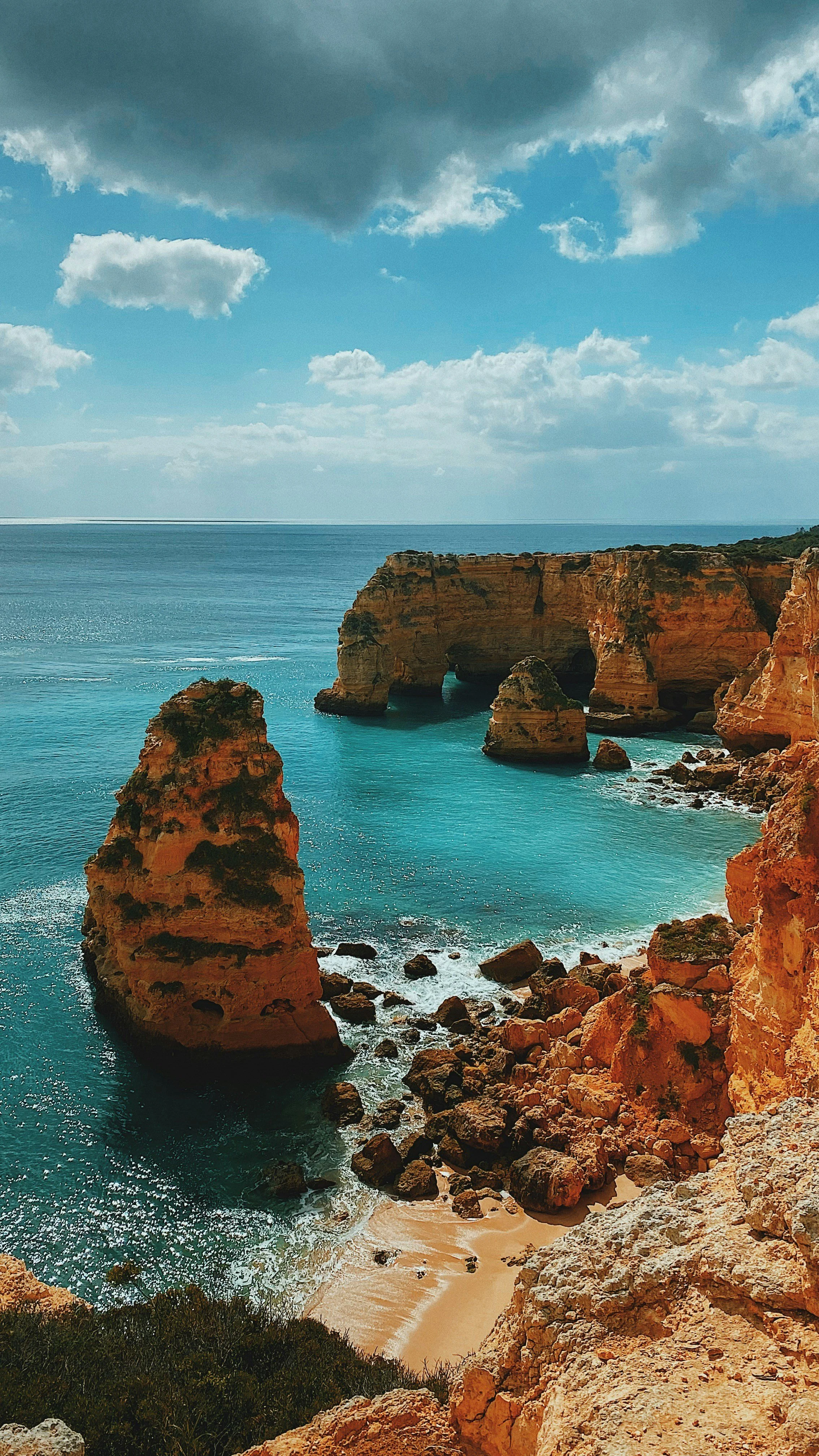 Felsformationen und Klippen an der Algarve-Küste mit einem Sandstrand und dem Atlantischen Ozean unter einem bewölkten Himmel.