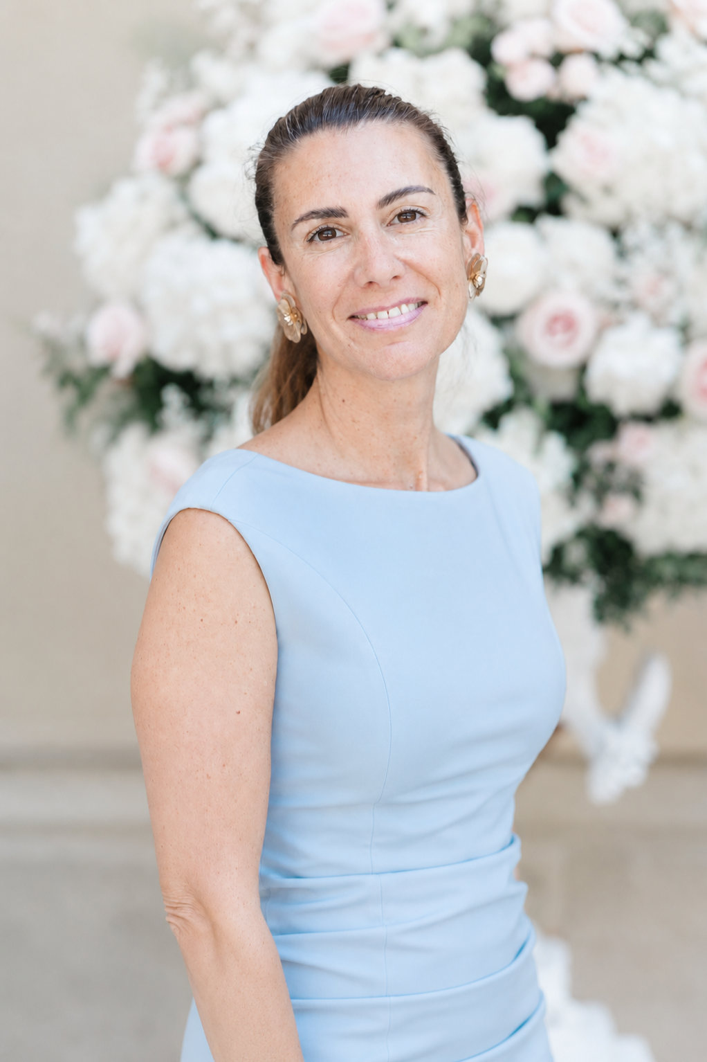 Eine Frau in einem hellblauen Kleid steht vor einem großen Blumenarrangement mit weißen und rosa Blumen.