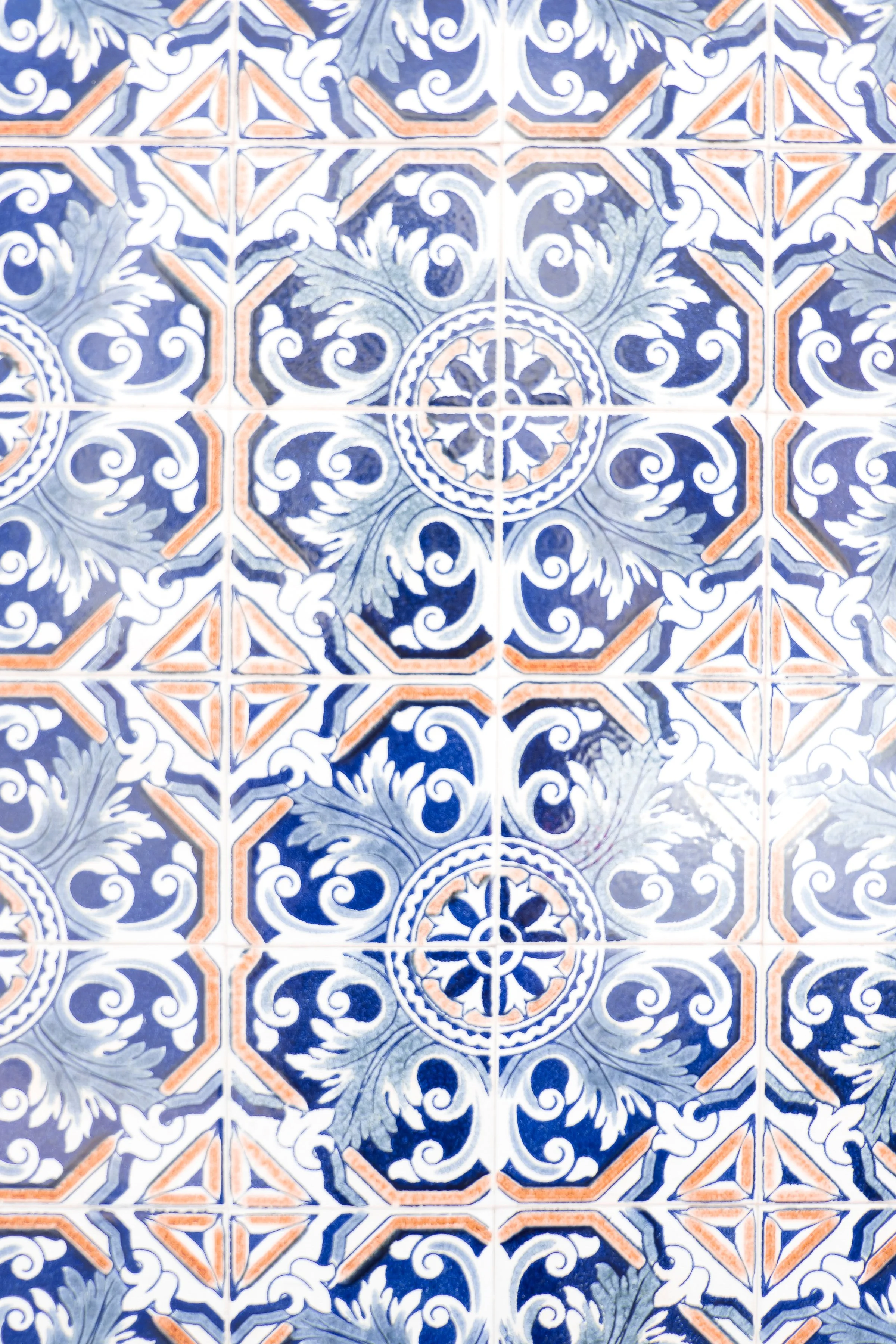 Bunte Fliesen mit blauen, weißen und orangefarbenen Mustern, floral und geometrisch, in einer quadratischen Anordnung.
