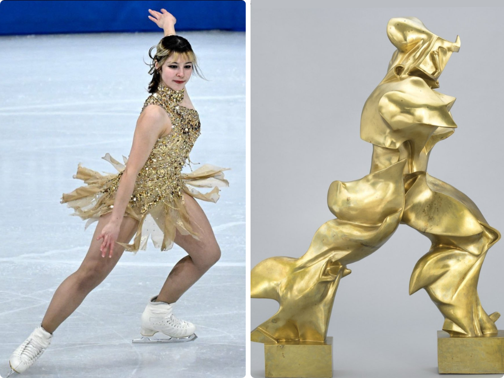 A female figure skater performing on ice in a gold costume, with an abstract gold sculpture beside her.