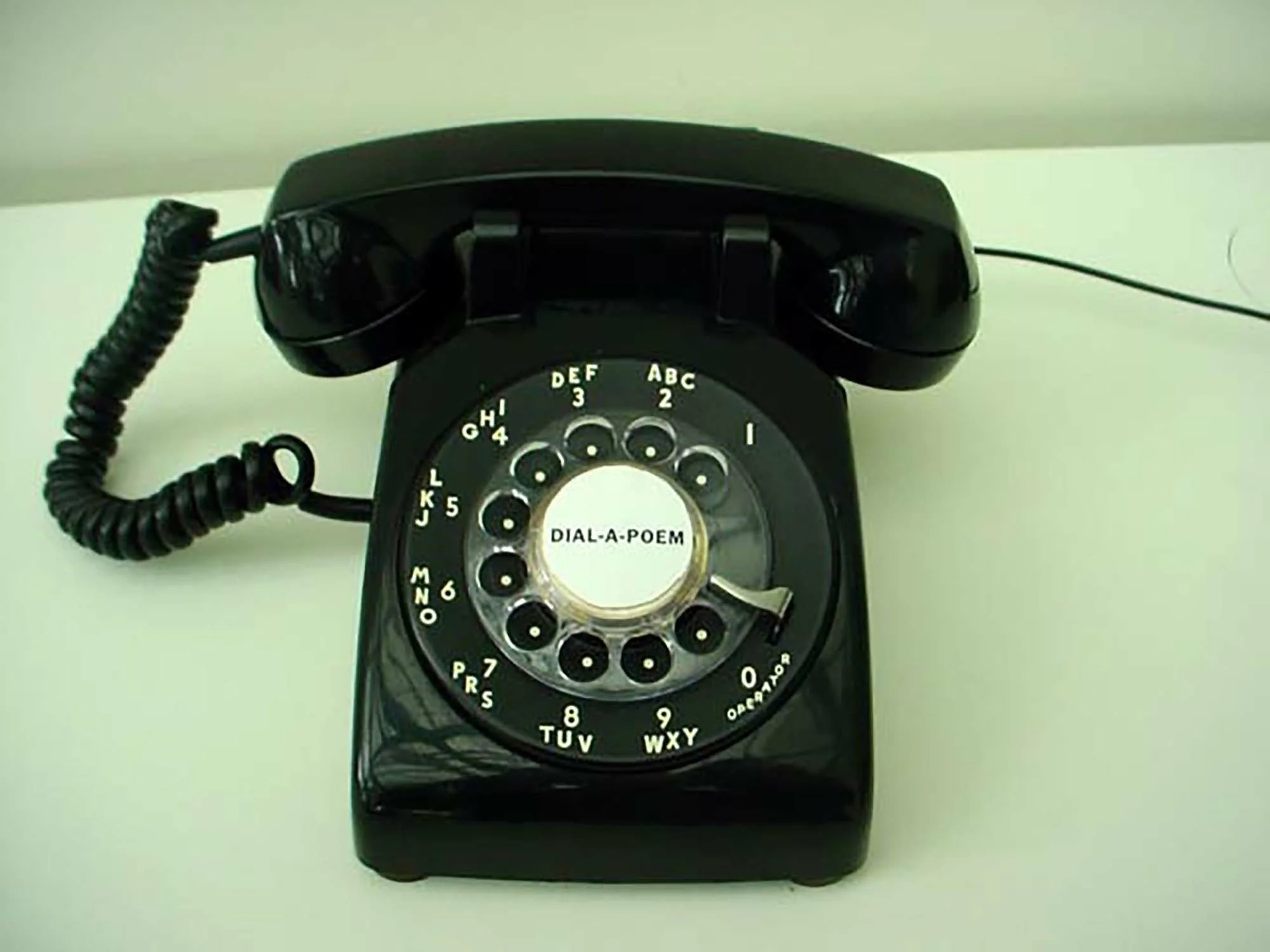 Vintage rotary dial telephone with a black body, coiled cord, and a circular dial with numbers and letters for dialing numbers.