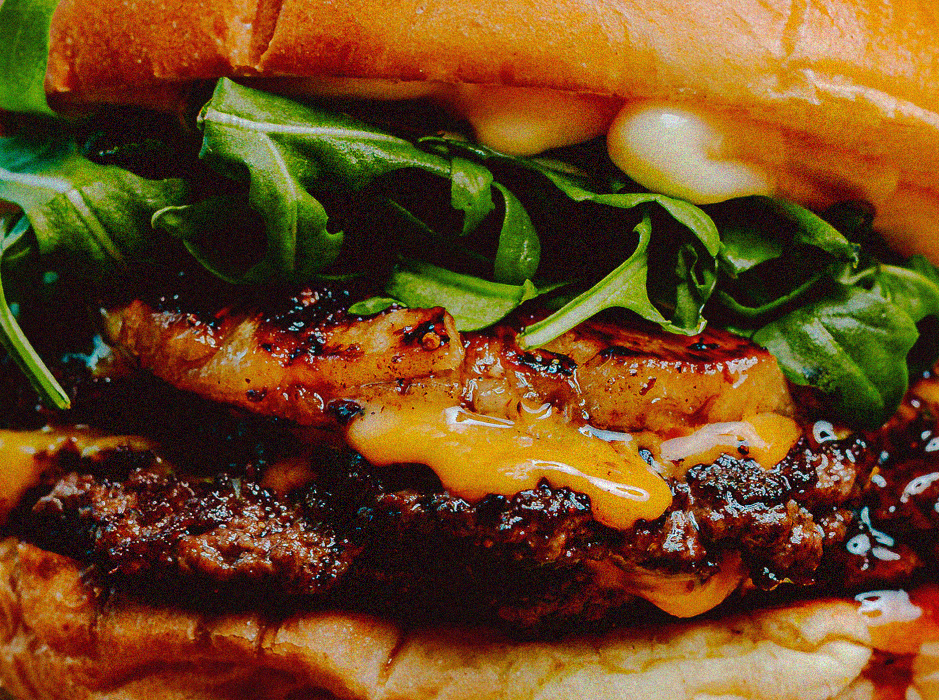 Close-up of a cheeseburger with leafy greens, melted cheese, and grilled meat patty.