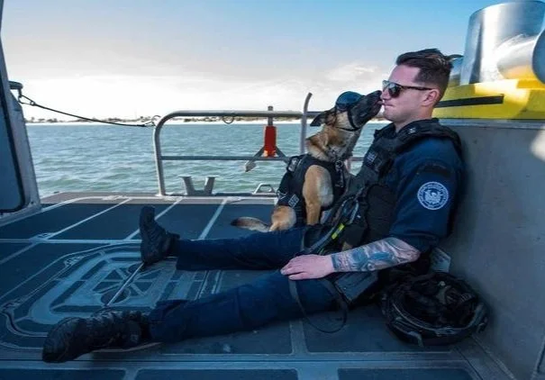 Coast Guard K9 handler sitting on a boat with his working dog.