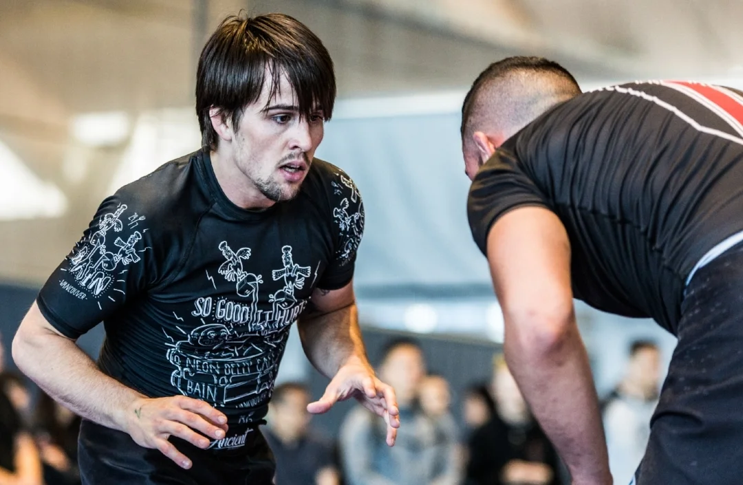 Two men engaged in a face-to-face wrestling match, focusing intently, with a blurred crowd in the background.