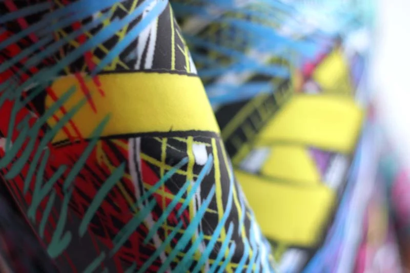 Close-up of a vibrant, patterned fabric with yellow, black, red, green, and purple colors and geometric designs.