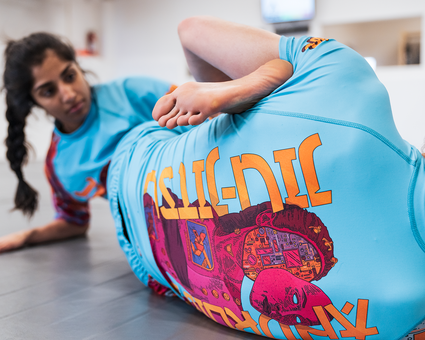 Young woman in a blue rash guard practicing a side plank on a black mat, focusing her gaze to the side.