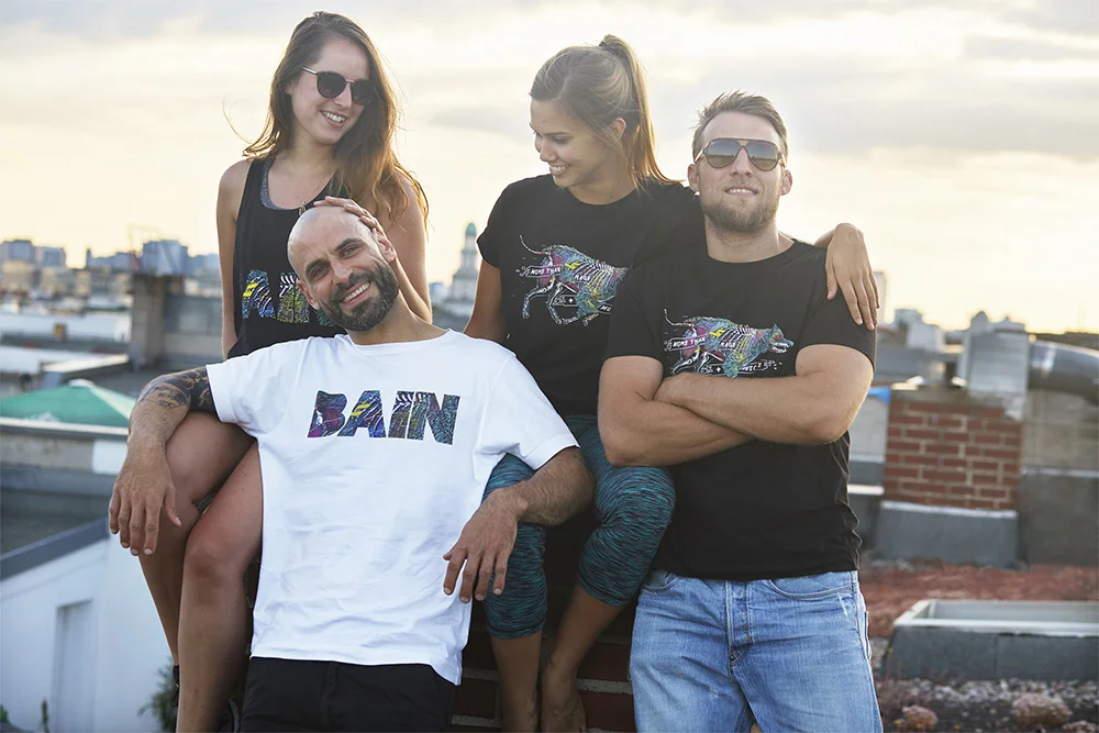 Four friends smiling and enjoying each other's company on a rooftop during sunset, with a cityscape in the background.