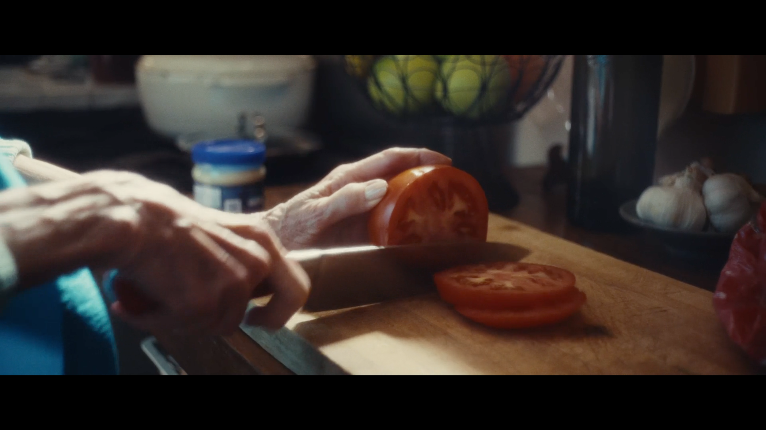 Person slicing a tomato on a wooden cutting board in a kitchen.