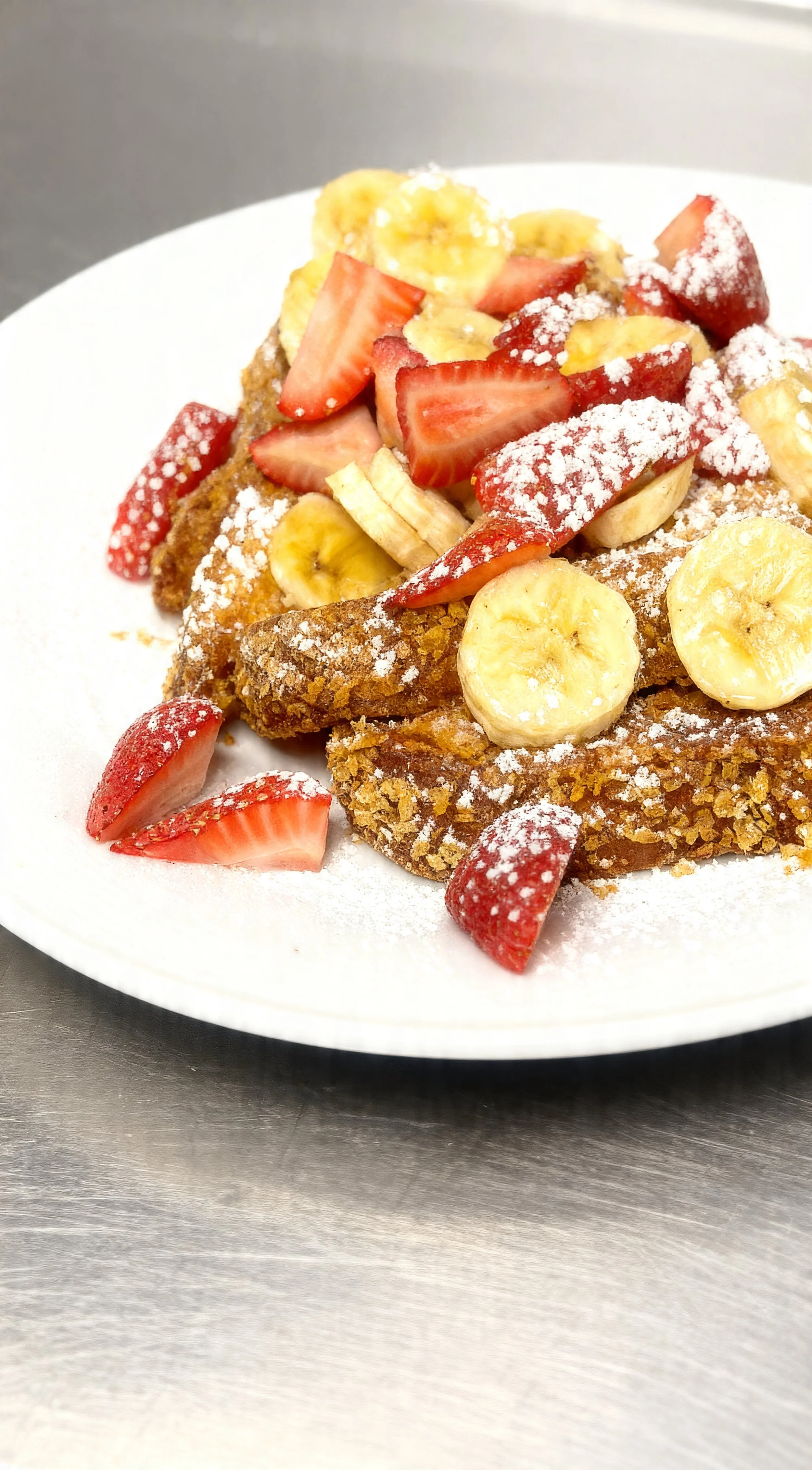 French toast topped with sliced strawberries and bananas, dusted with powdered sugar, served on a white plate.