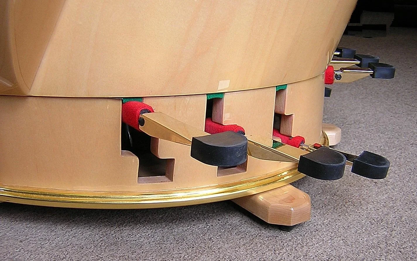 Close-up of a harp pedal box, showing the pedalss, on a carpeted floor.
