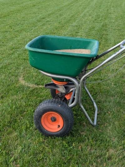 Green garden cart filled with sand on a grassy lawn.