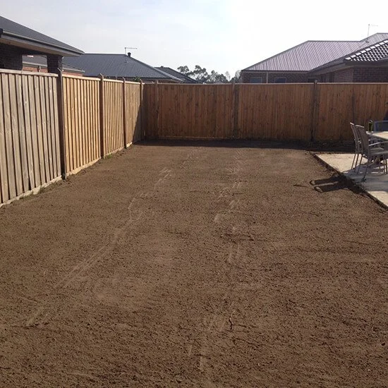 A backyard with a dirt yard and a wooden fence, with houses and rooftops visible in the background.